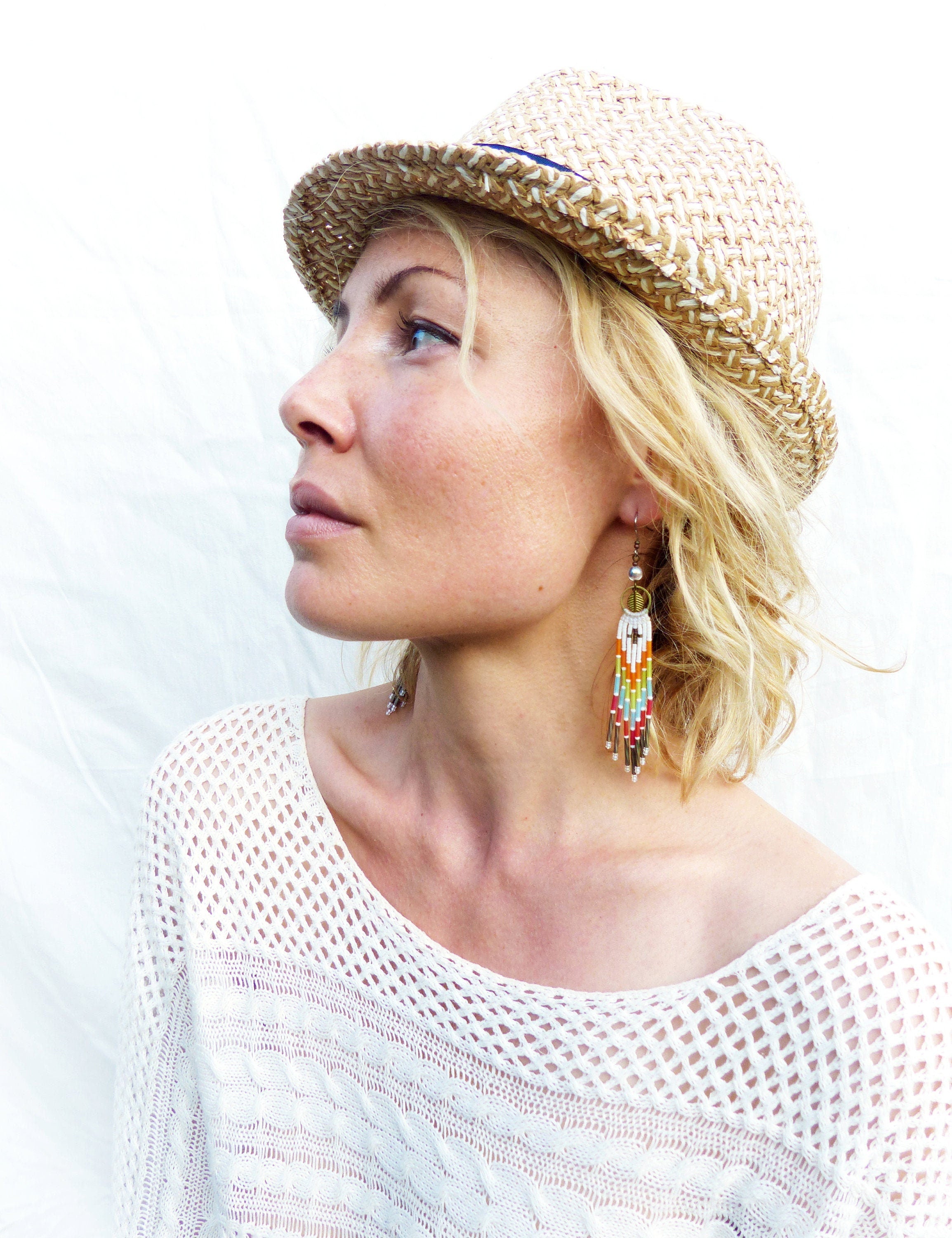 Peut inclure: Une femme portant un haut en crochet blanc et un fedora en paille avec un bandeau bleu. Elle porte des boucles d'oreilles en perles colorées.