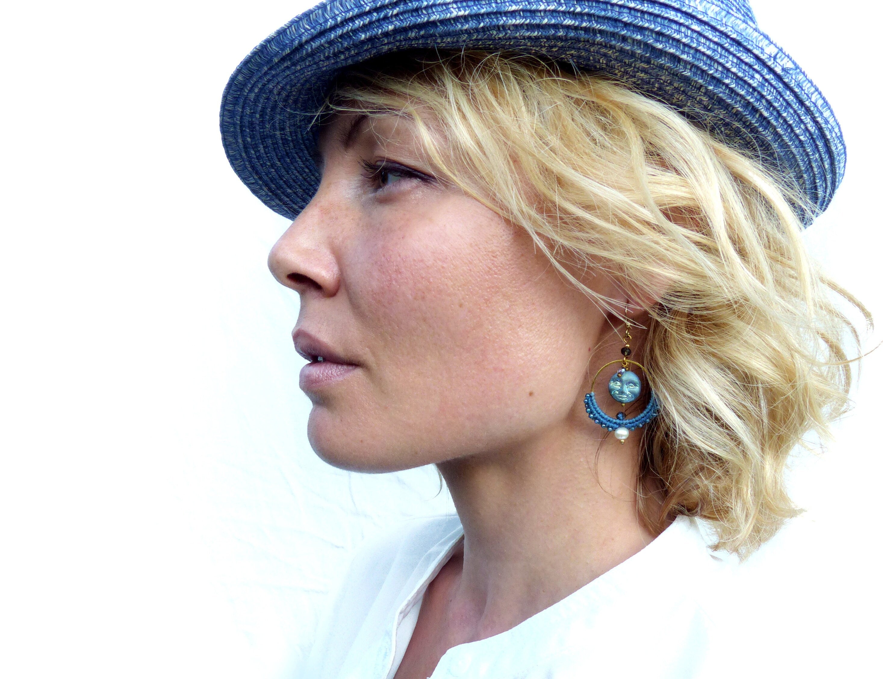 Peut inclure: Une femme aux cheveux blonds portant un chapeau de paille bleu et des boucles d'oreilles bleues et dorées avec un accent de perle. 