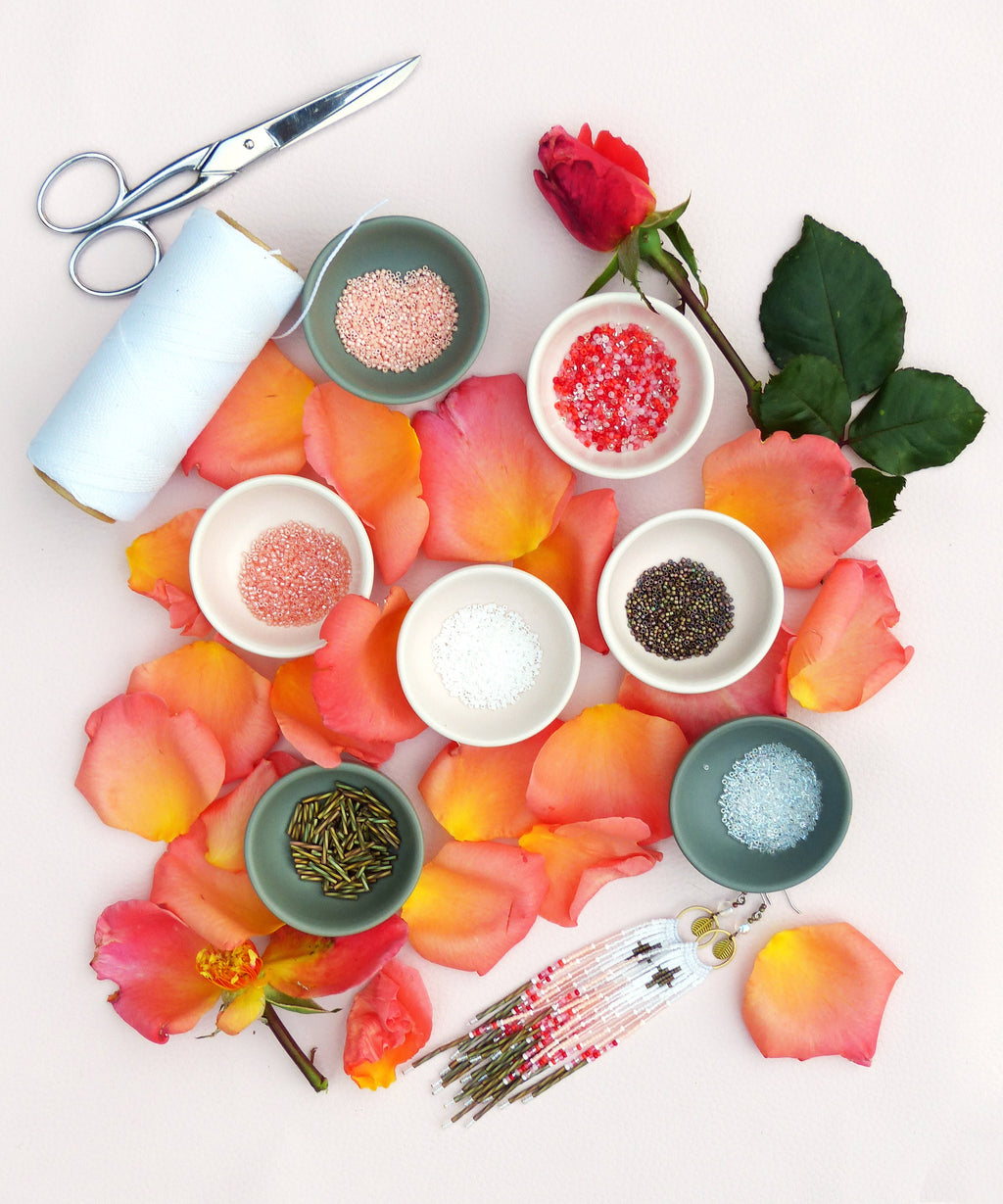 Peut inclure: Un ensemble de perles colorées dans de petits bols, entourées de pétales de rose, avec une paire de boucles d'oreilles en perles et une bobine de fil. 