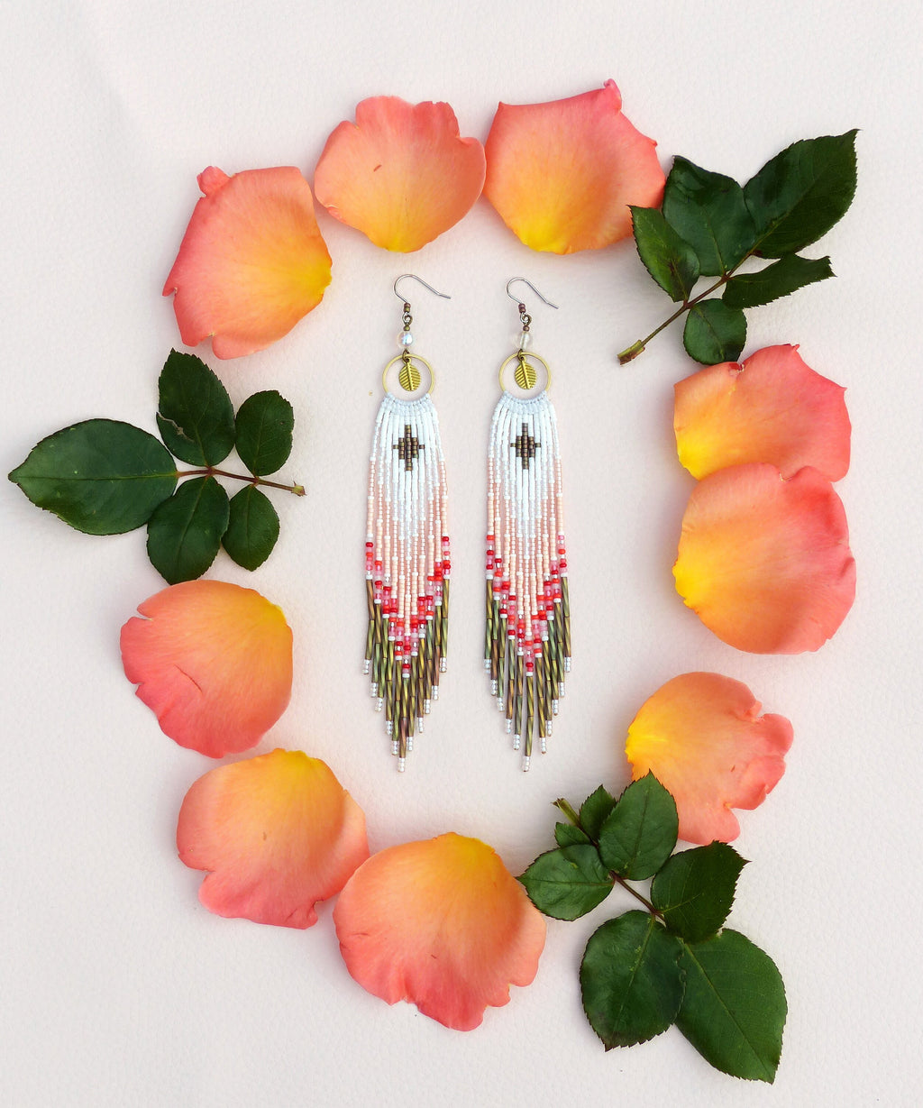 Peut inclure: Une paire de longues boucles d'oreilles en perles avec un motif géométrique et un petit pendentif en forme de croix au sommet. Les perles sont de couleur blanche, rose et verte.