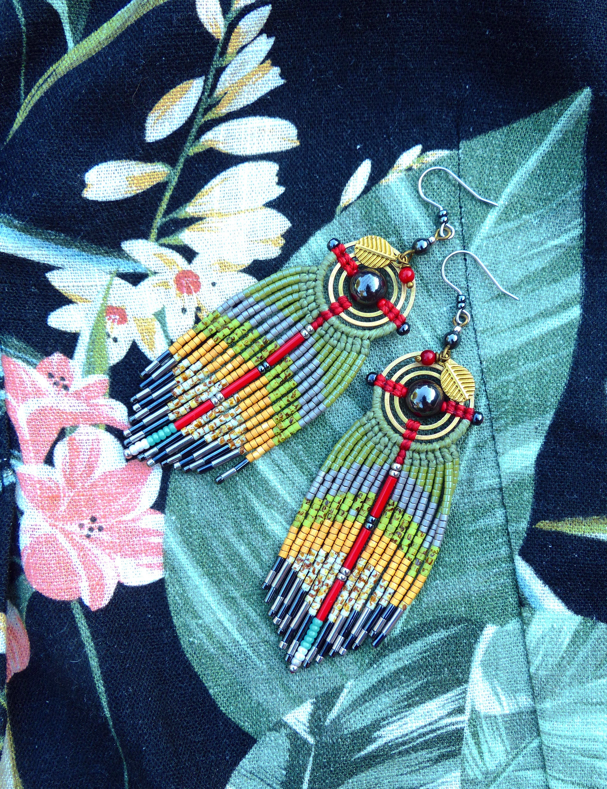 Peut inclure: Une paire de longues boucles d'oreilles en perles avec un schéma de couleurs vert, jaune et rouge. Les boucles d'oreilles présentent un motif circulaire avec une pierre sombre au centre et un accent en feuille d'or.