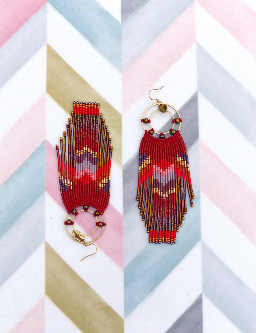 Peut inclure: Une paire de longues boucles d'oreilles en perles avec un motif rouge, or et violet. Les boucles d'oreilles présentent un anneau circulaire avec un petit charme en forme de feuille.