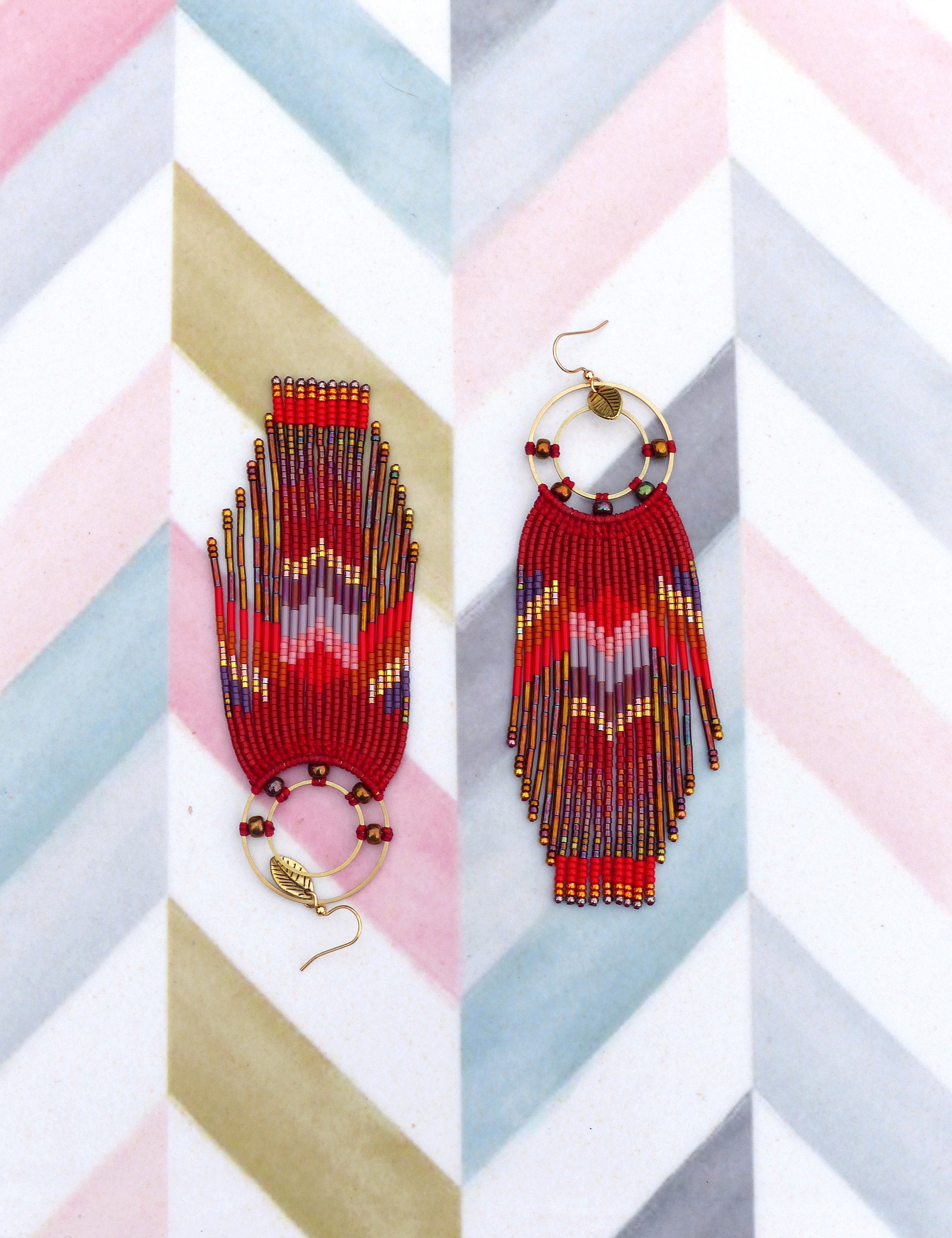 Peut inclure: Une paire de longues boucles d'oreilles en perles avec un motif rouge, or et violet. Les boucles d'oreilles présentent un anneau circulaire avec un petit charme en forme de feuille.