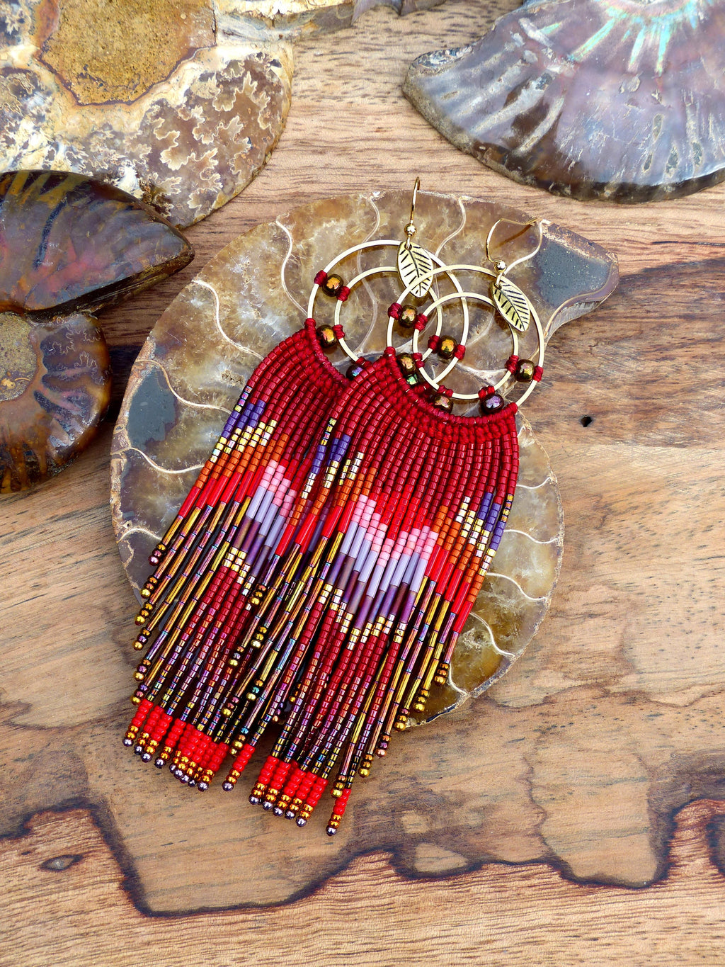 Peut inclure: Boucles d'oreilles en franges de perles rouges, orange, dorées et violettes avec des cercles dorés et des breloques en forme de feuilles.
