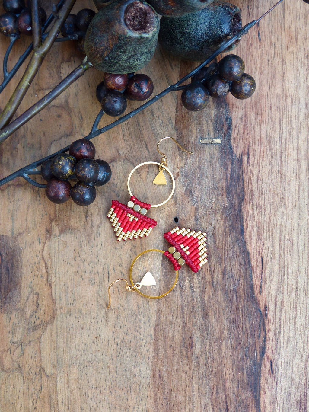 Peut inclure: Une paire de boucles d'oreilles en perles rouges et dorées avec un charme triangulaire suspendu à un anneau doré.