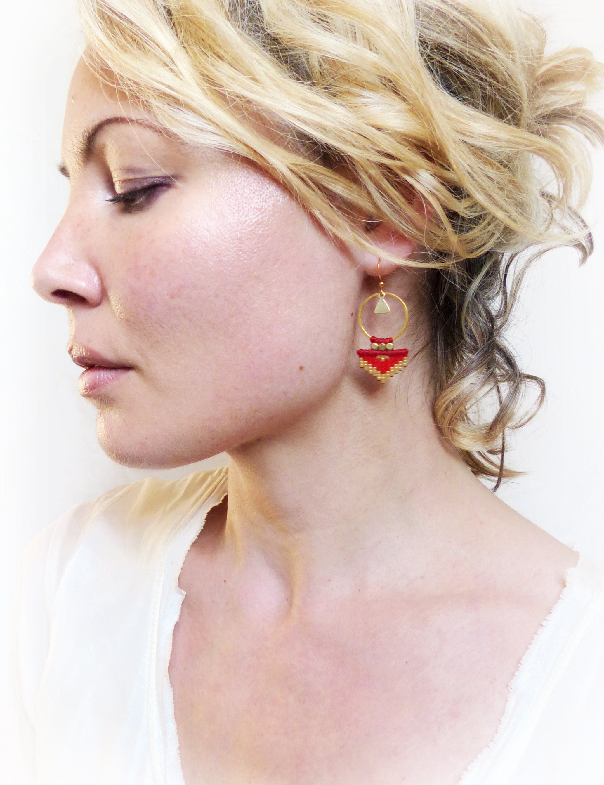Peut inclure: Une paire de boucles d'oreilles en or avec un motif géométrique rouge. Les boucles d'oreilles présentent une petite forme triangulaire avec un cercle au-dessus.