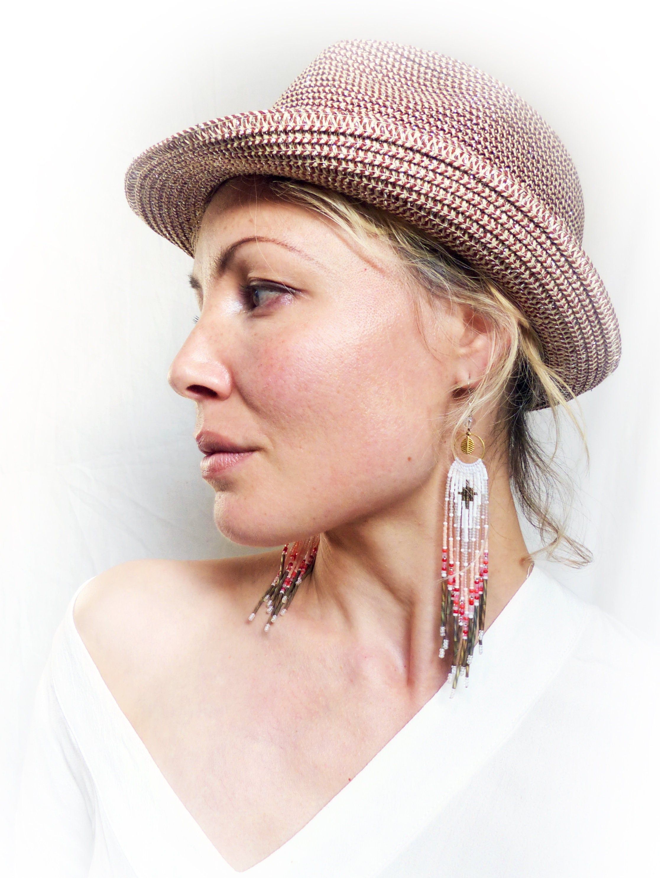 Peut inclure: Une femme portant un chapeau de paille brun et blanc avec de longues boucles d'oreilles en perles. Les boucles d'oreilles sont blanches avec des accents rouges et bruns.