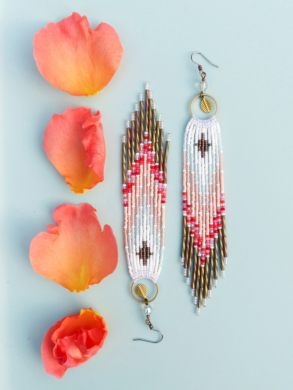 Peut inclure: Une paire de longues boucles d'oreilles en perles avec un motif géométrique dans des tons de rouge, rose et blanc. Les boucles d'oreilles ont un charme en forme de feuille dorée et une fermeture à crochet.