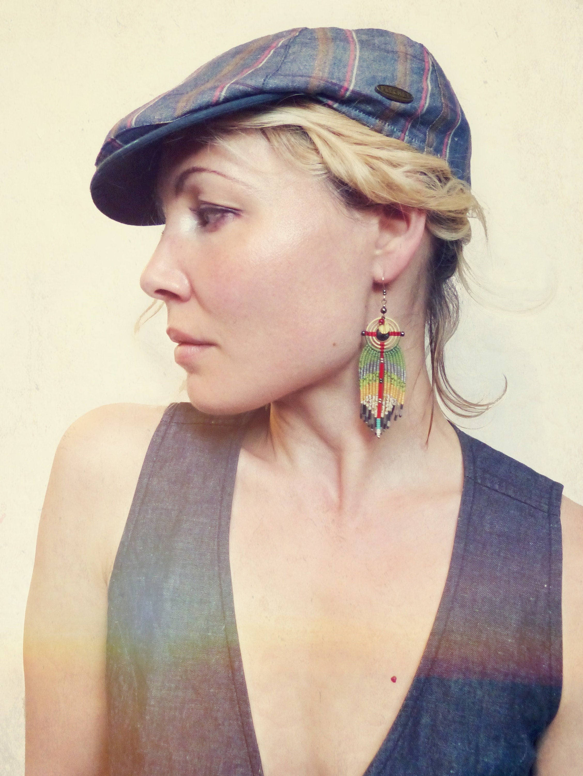 Peut inclure: Une femme portant une casquette à motif gris et bleu et un haut gris sans manches avec un décolleté en V profond. Elle porte une longue boucle d'oreille en perles colorées avec un motif circulaire.