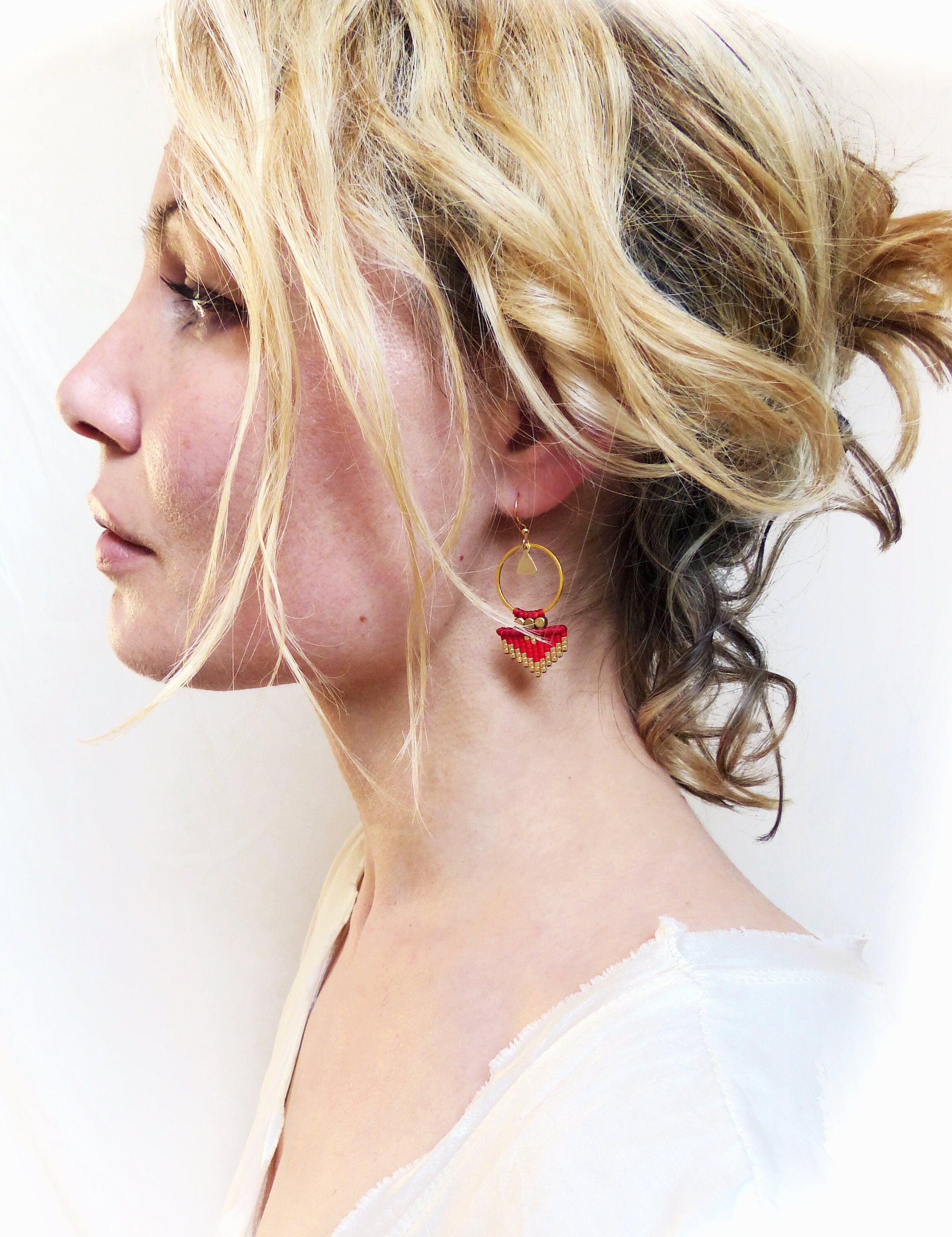 Peut inclure: Une paire de boucles d'oreilles créoles dorées avec un pendentif géométrique rouge et or. Les boucles d'oreilles pendent du lobe de l'oreille.