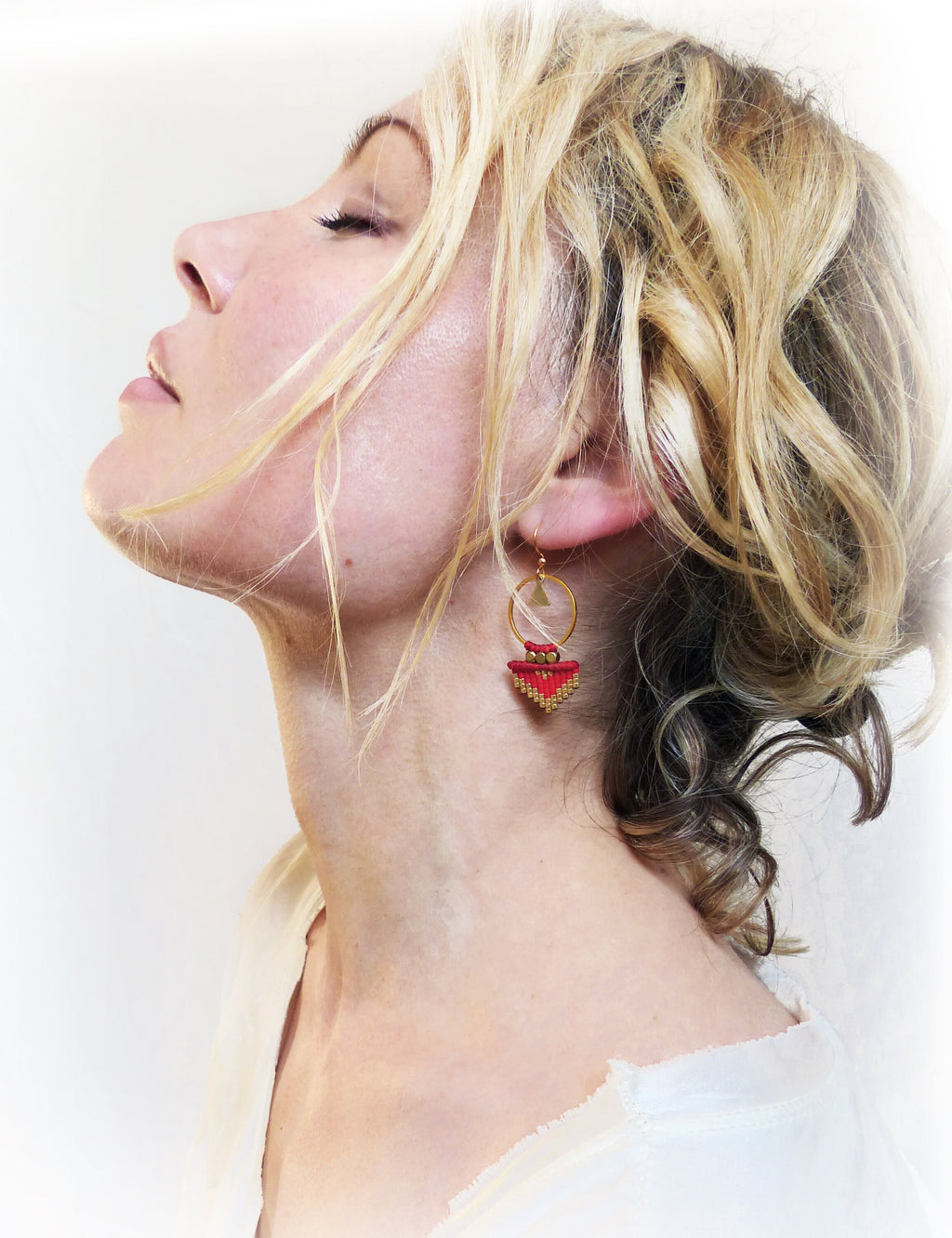 Peut inclure: Une paire de boucles d'oreilles créoles dorées avec un pendentif géométrique rouge et or. Le pendentif est fait de petites perles et a une forme triangulaire.