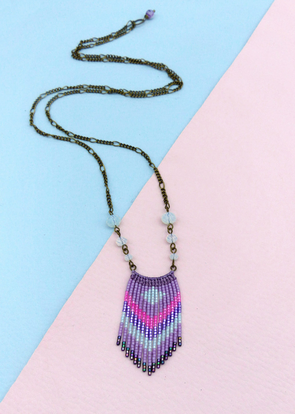Peut inclure: Un collier en perles violettes et roses avec un motif en frange. Le collier est fait de petites perles et a une chaîne en bronze.