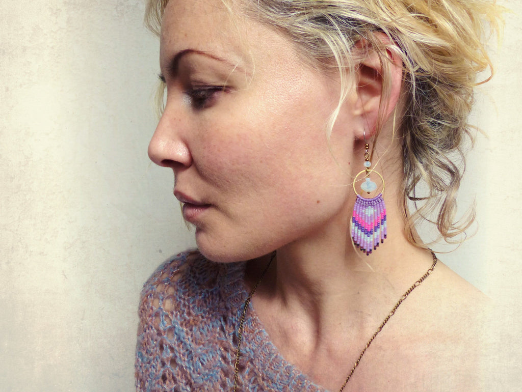 Peut inclure: Une femme portant un pull en tricot bleu et violet avec une paire de longues boucles d'oreilles en perles. Les boucles d'oreilles sont faites de perles roses, violettes et bleues et ont un anneau en or en haut. Les boucles d'oreilles pendent de son oreille gauche.