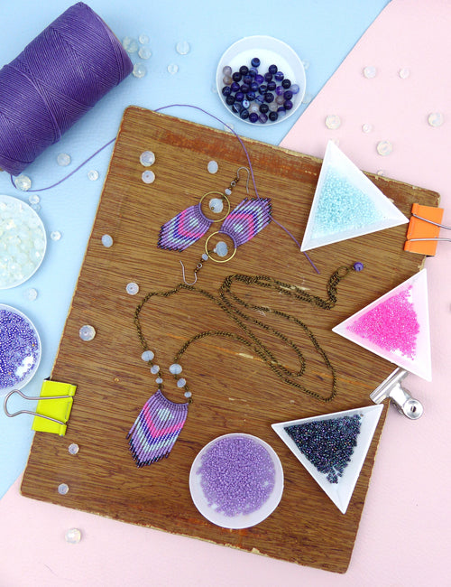 Peut inclure: Un plateau en bois avec divers perles et fournitures de bijouterie. Il y a de petits bols de perles en violet, rose, bleu et noir. Il y a aussi des boucles d'oreilles et un collier faits de perles dans des tons de violet, rose et bleu.