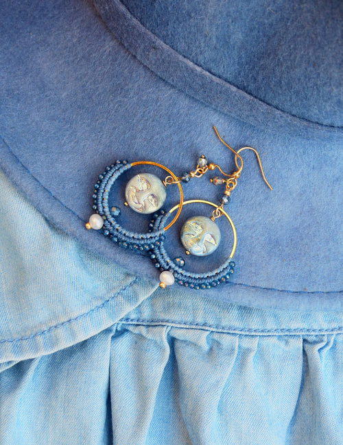 Peut inclure: Une paire de boucles d'oreilles créoles bleues et dorées avec une perle de verre bleue et blanche au centre de chaque créole.