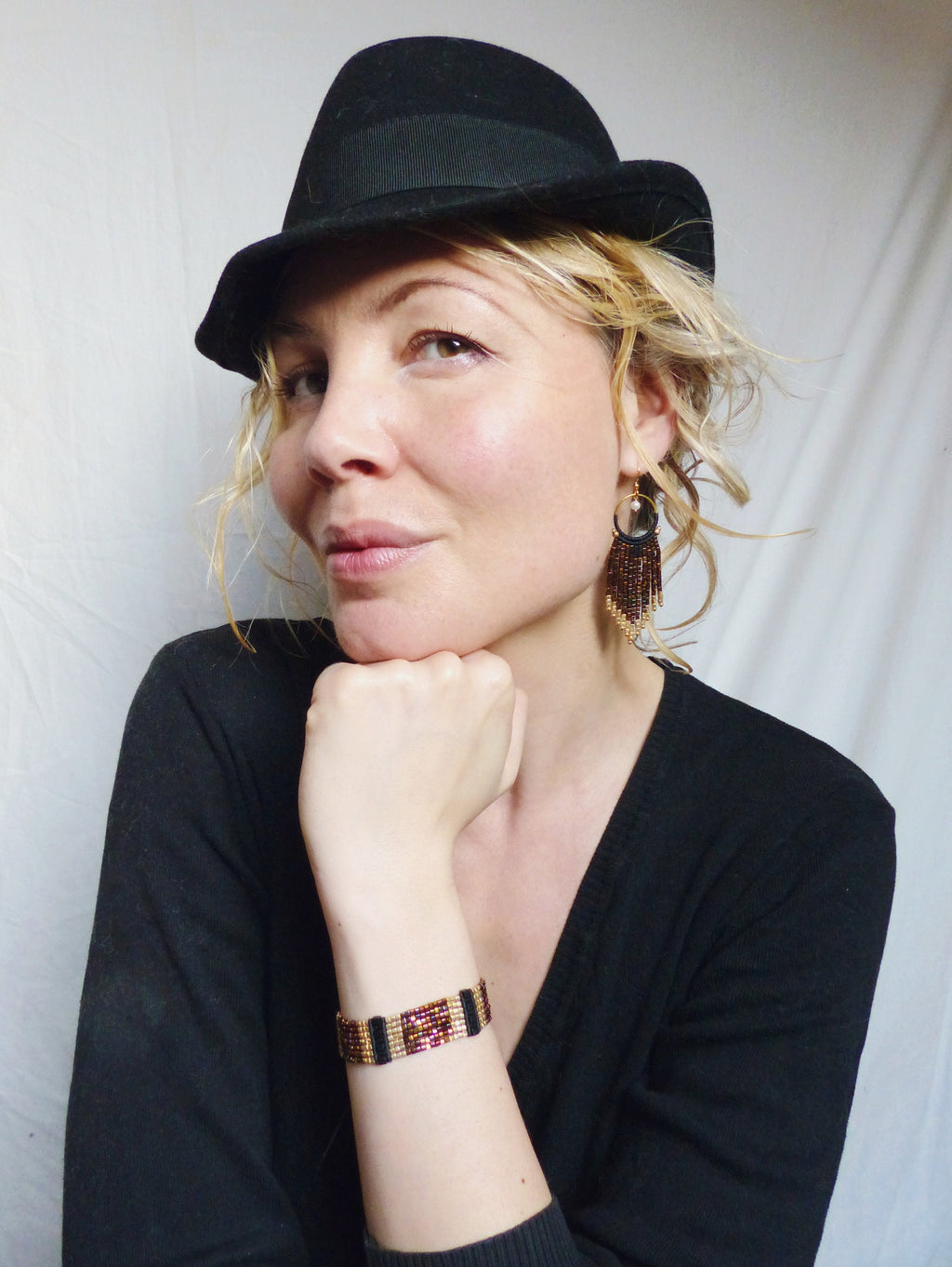 Peut inclure: Une femme portant un chapeau fedora noir avec un bracelet en perles noires et dorées au poignet. Elle porte un haut noir et a de longs cheveux bruns.