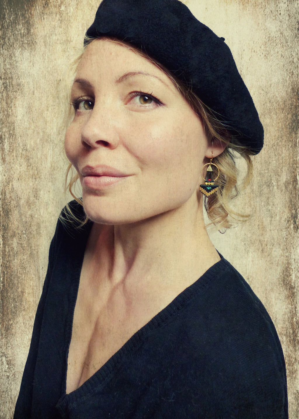 Peut inclure: Une femme portant un béret noir et un pull noir à col bas. Elle porte des boucles d'oreilles dorées avec des perles noires et vertes.