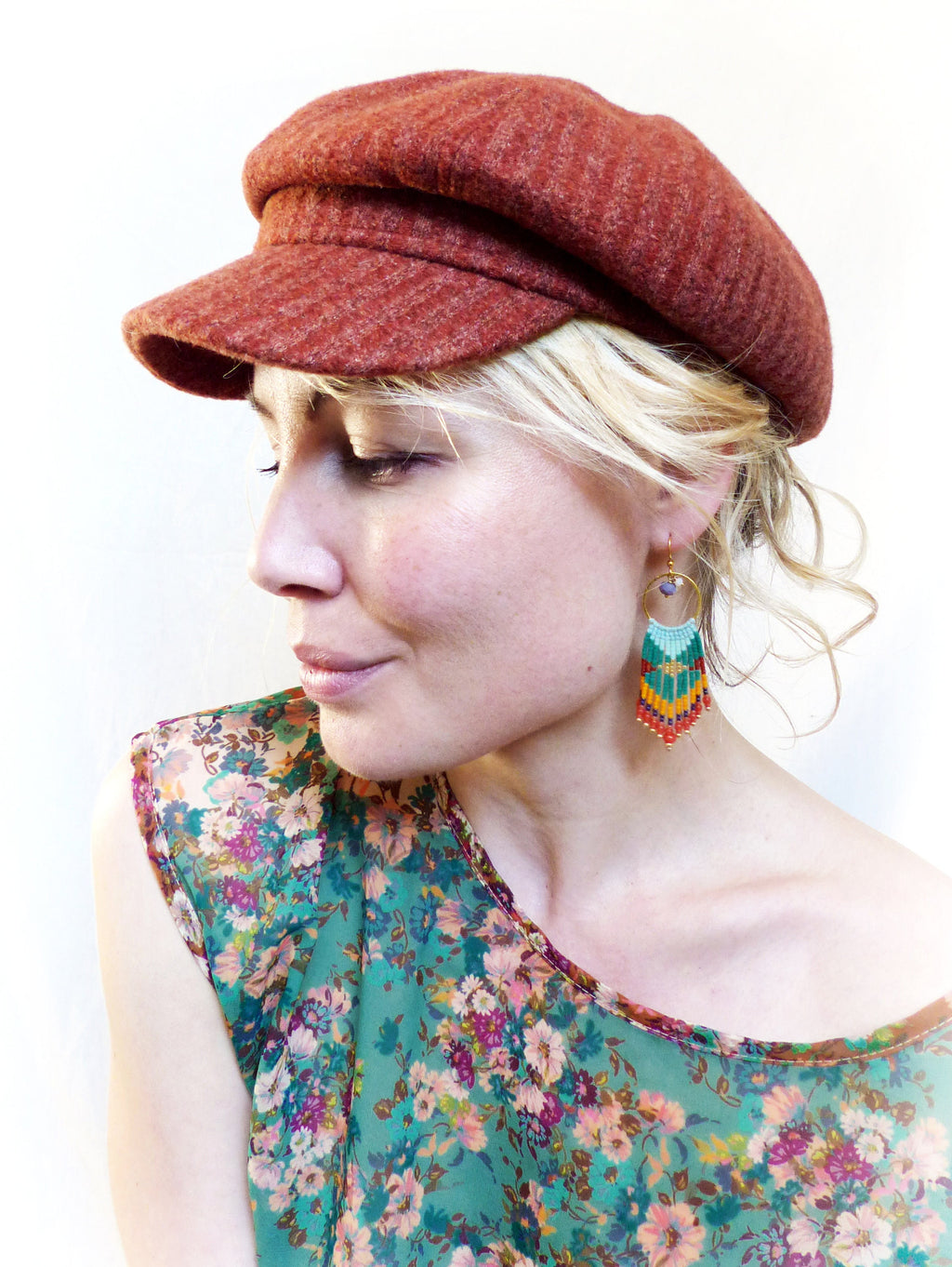 Peut inclure: Une femme portant une casquette de newsboy rouge et une blouse à imprimé floral avec des boucles d'oreilles pendantes en perles. Les boucles d'oreilles sont vertes, bleues et orange.