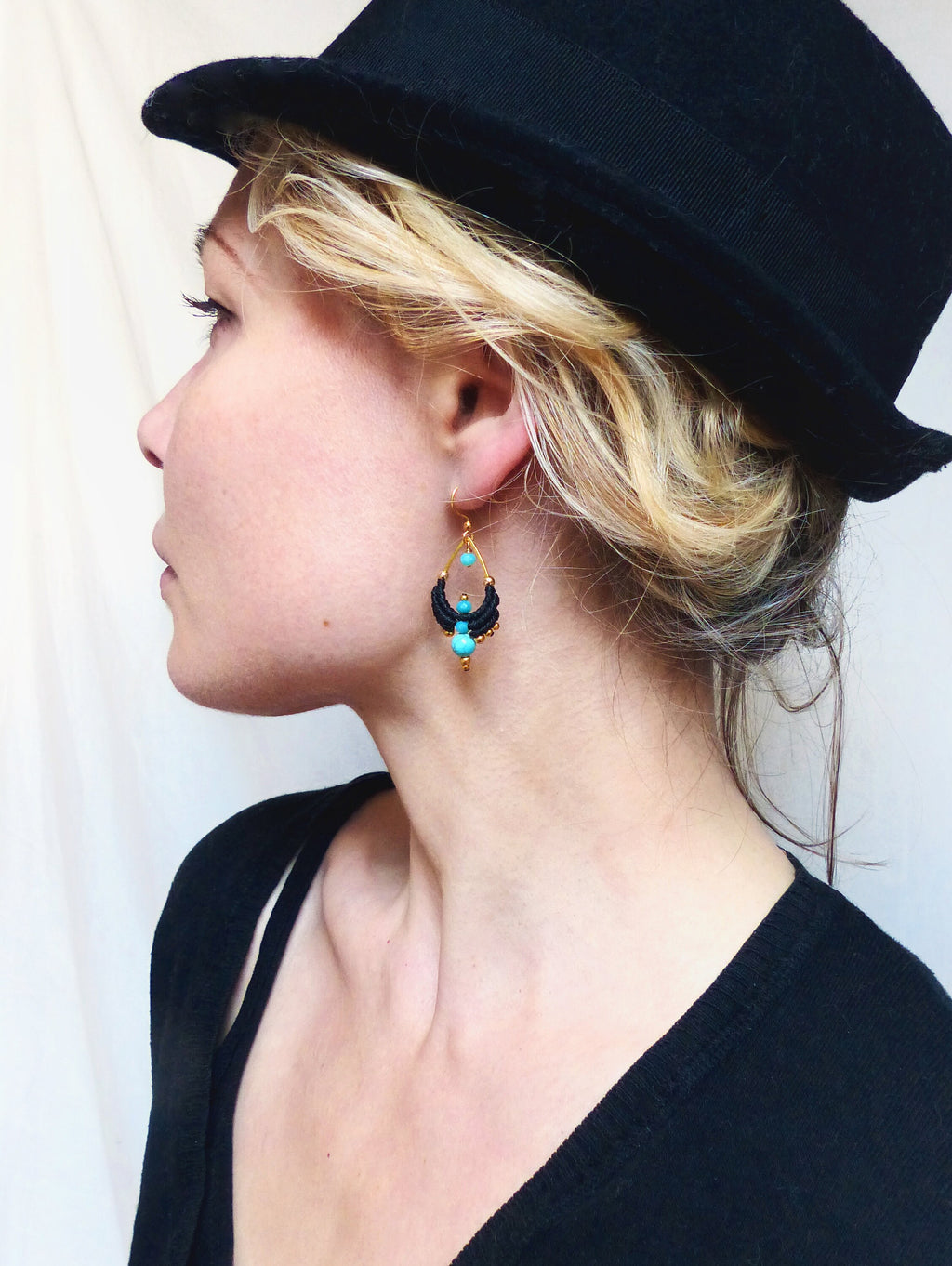 Peut inclure: Une femme portant un fedora noir et un pull noir avec des boucles d'oreilles turquoise et dorées. Les boucles d'oreilles sont faites de petites perles et ont une forme de larme.