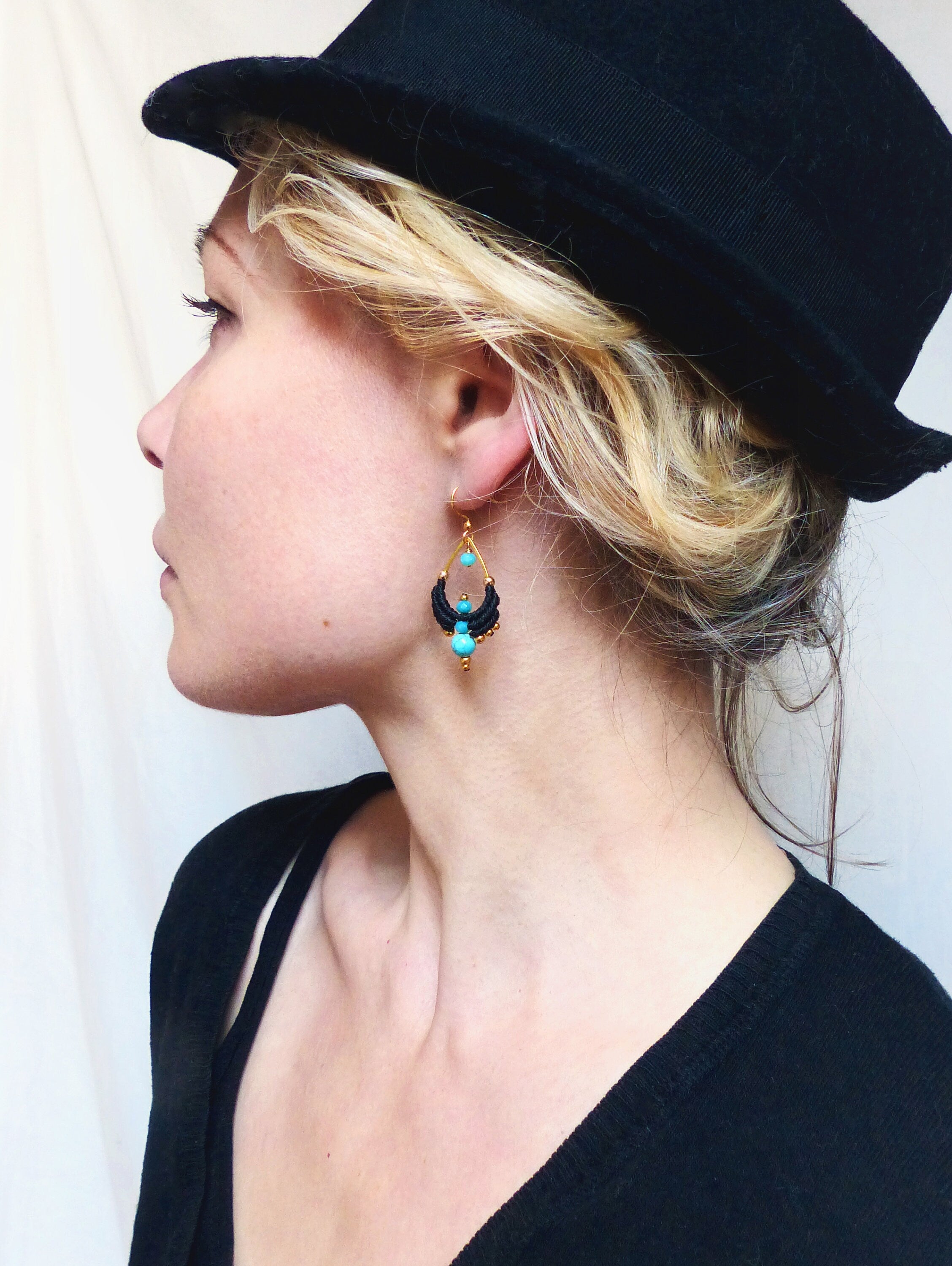 Peut inclure: Une femme portant un fedora noir et un pull noir avec des boucles d'oreilles turquoise et dorées. Les boucles d'oreilles sont faites de petites perles et ont une forme de larme.