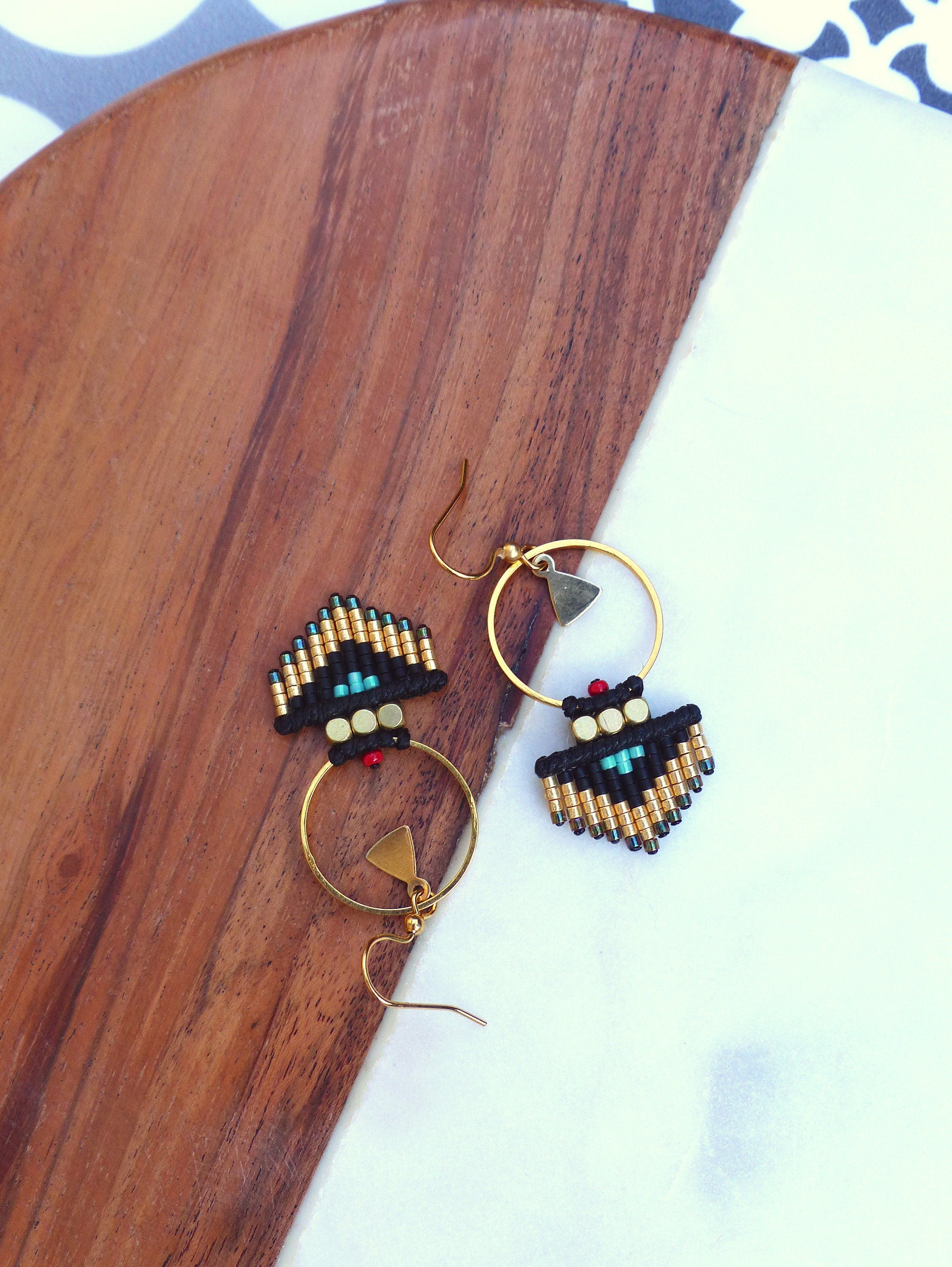 Peut inclure: Une paire de boucles d'oreilles créoles dorées avec des franges de perles noires et dorées. Les franges comportent des perles turquoise et rouges.