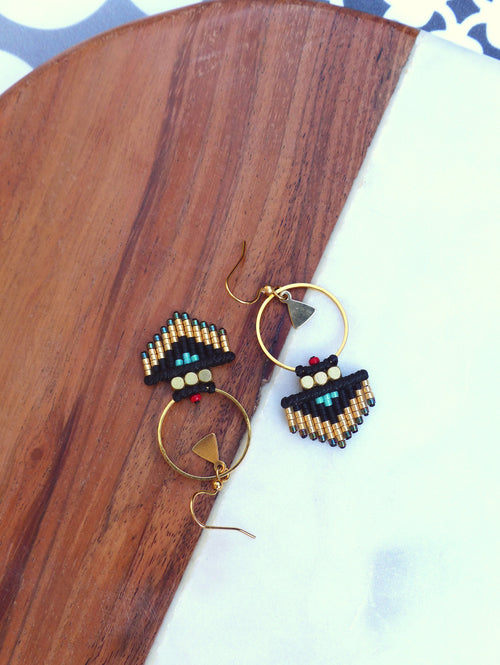 Peut inclure: Une paire de boucles d'oreilles créoles dorées avec des franges de perles noires et dorées. Les franges comportent des perles turquoise et rouges.