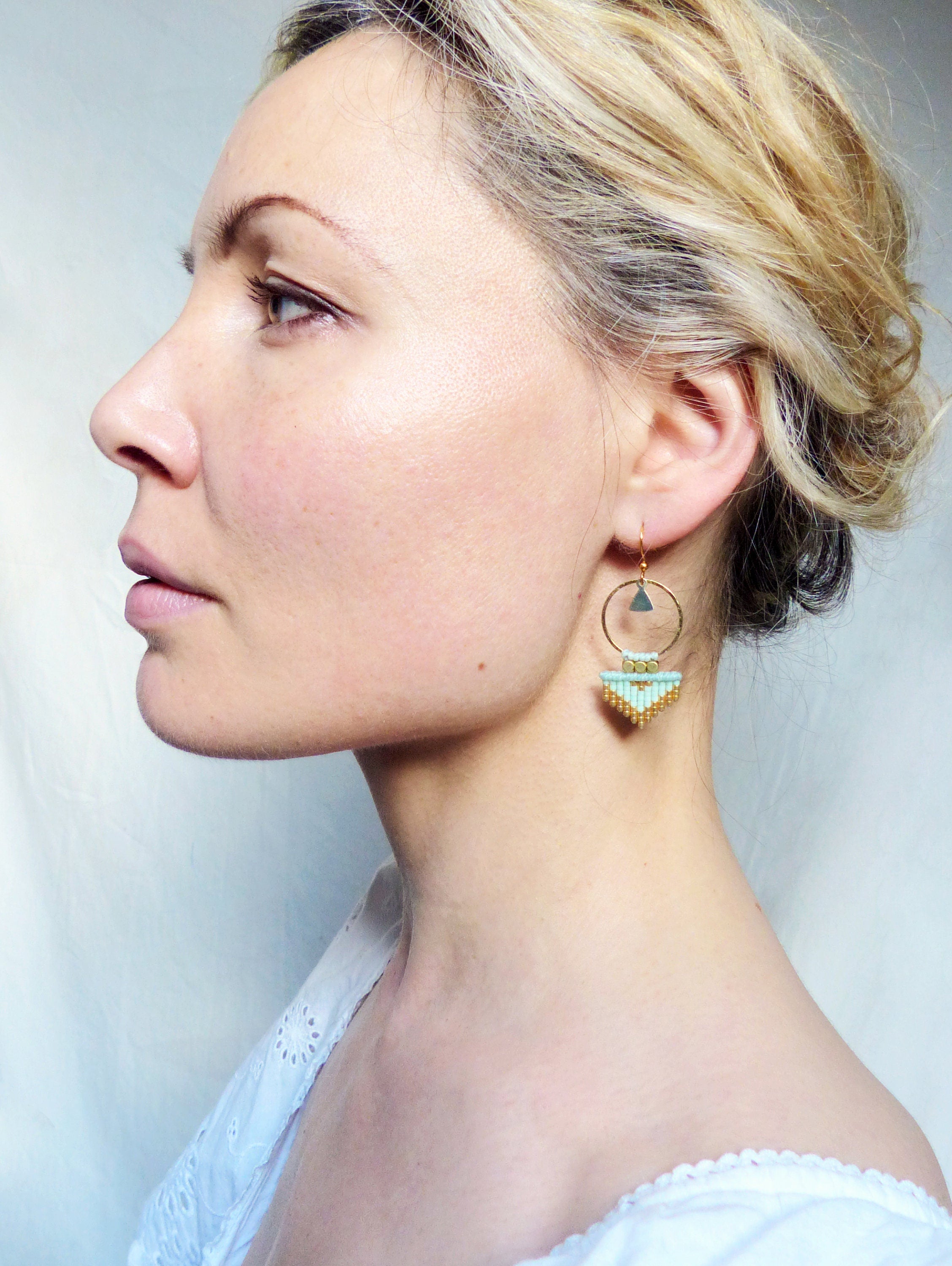 Peut inclure: Une paire de boucles d'oreilles créoles dorées avec un pendentif triangulaire en perles turquoise et dorées.