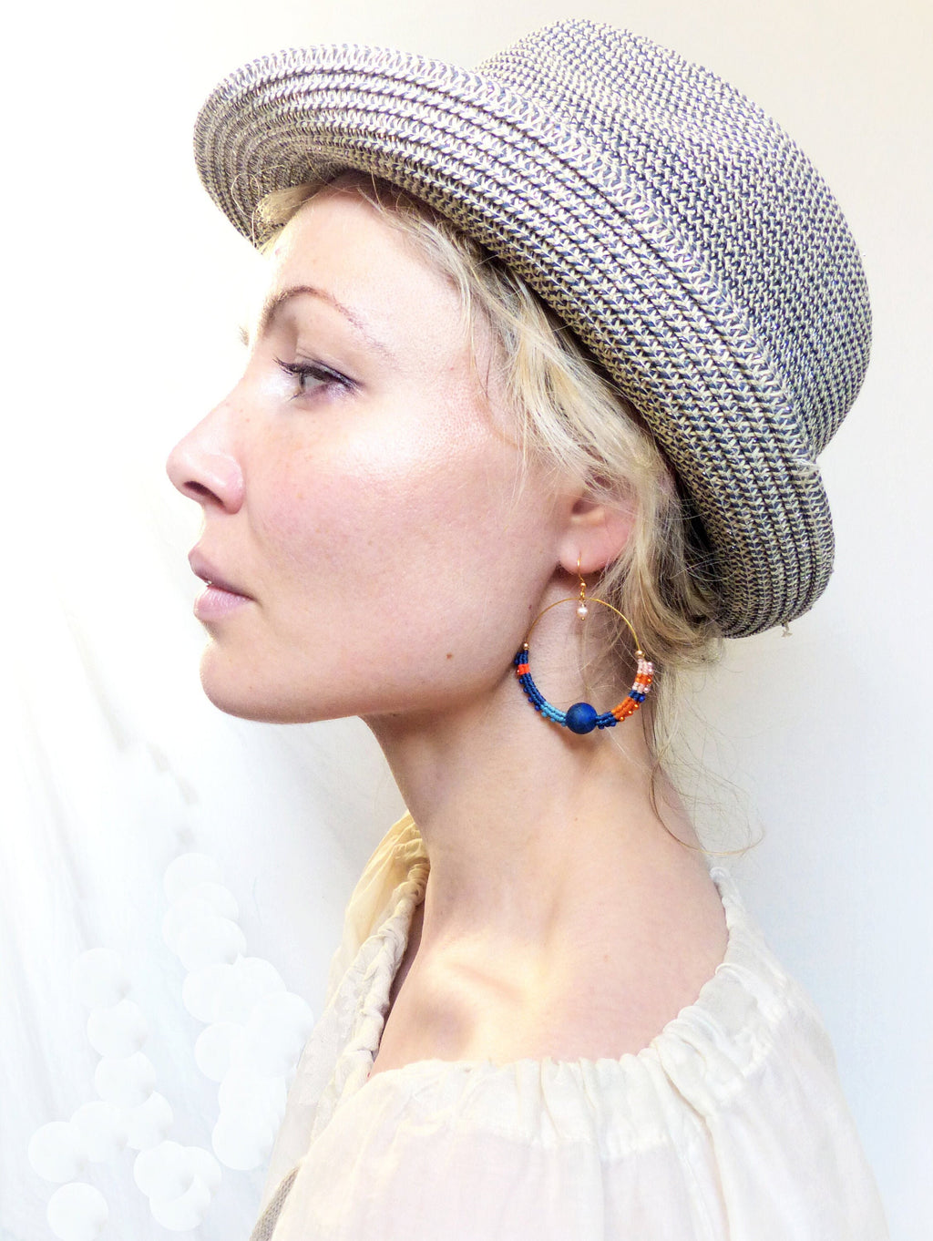 Peut inclure: Une femme portant un chapeau de paille et un haut blanc avec une paire de boucles d'oreilles créoles en perles bleues, orange et roses.