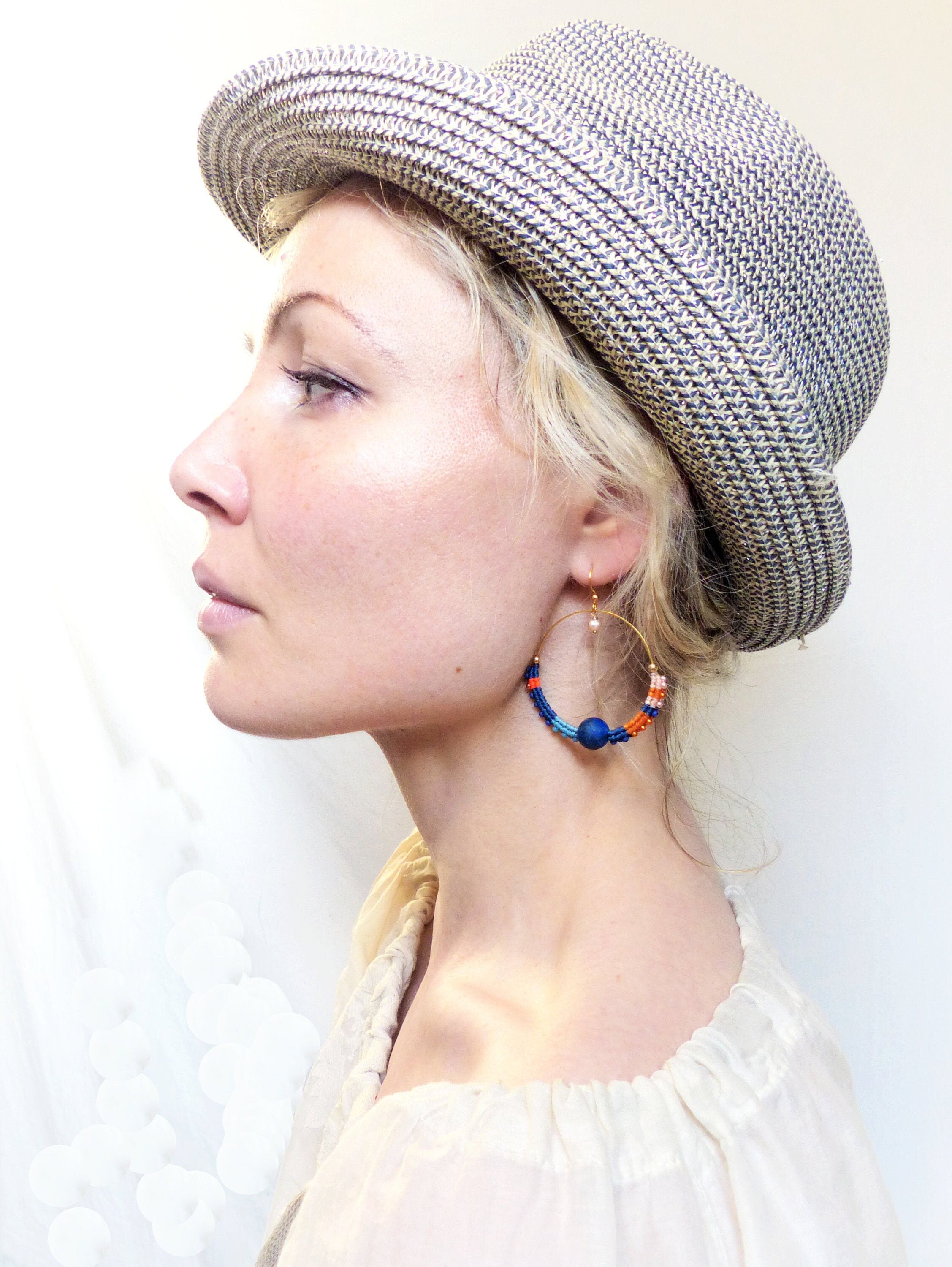 Peut inclure: Une femme portant un chapeau de paille et un haut blanc avec une paire de boucles d'oreilles créoles en perles bleues, orange et roses.