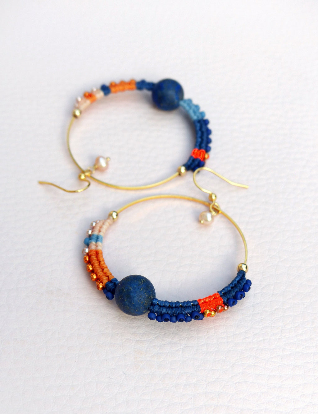 Peut inclure: Une paire de boucles d'oreilles créoles dorées avec un motif de perles bleues et orange. Chaque boucle d'oreille est ornée d'une grosse perle bleue.