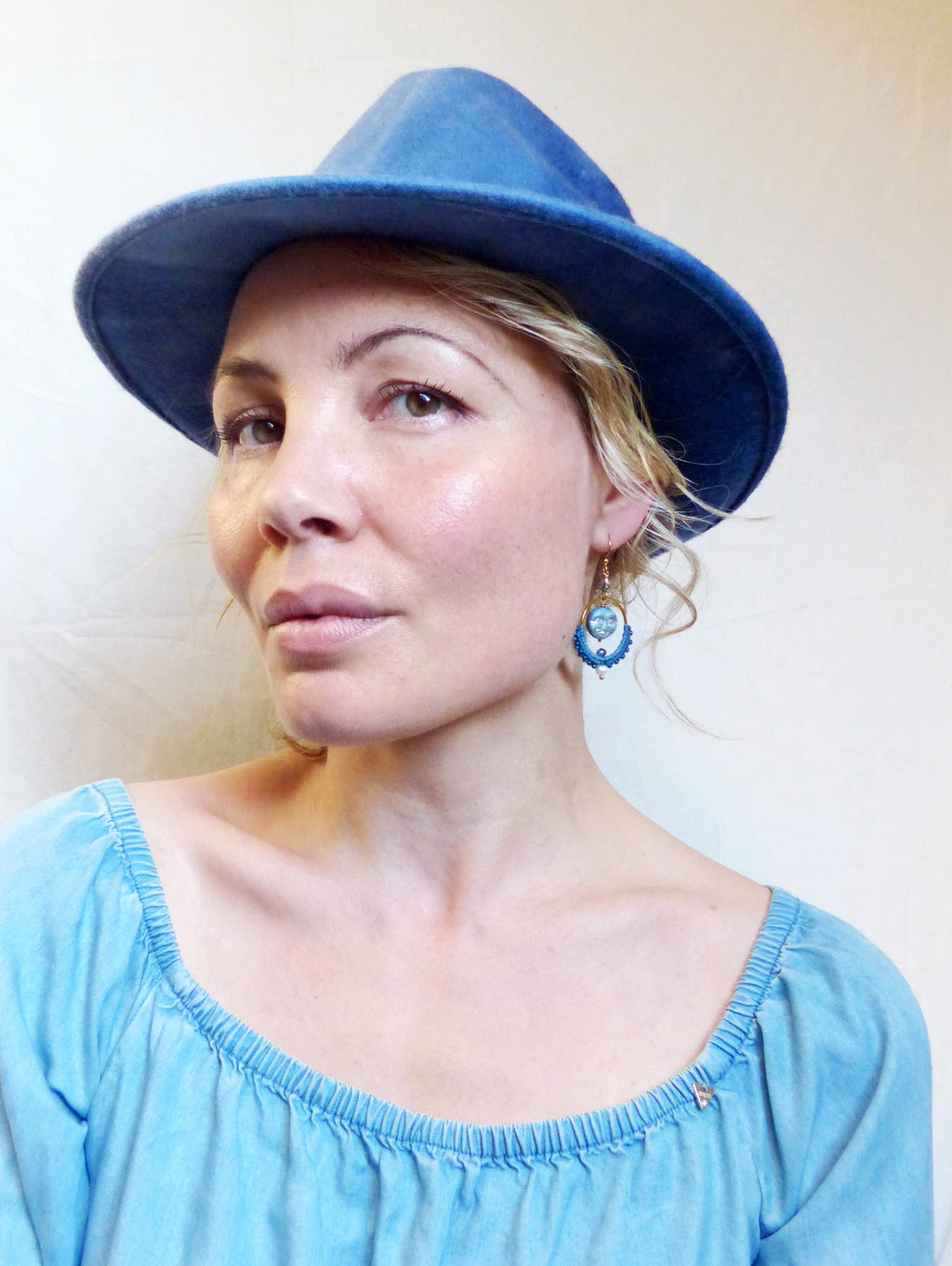 Peut inclure: Une femme portant un chapeau en jean bleu et un haut bleu clair à épaules dénudées. Elle porte des boucles d'oreilles bleues et dorées.