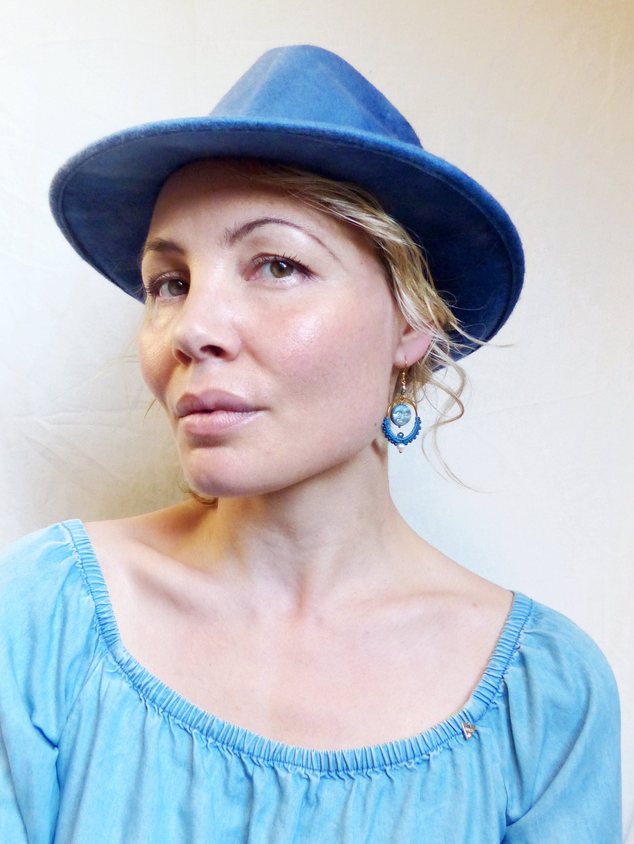 Peut inclure: Une femme portant un chapeau en jean bleu et un haut bleu clair à épaules dénudées. Elle porte des boucles d'oreilles bleues et dorées.