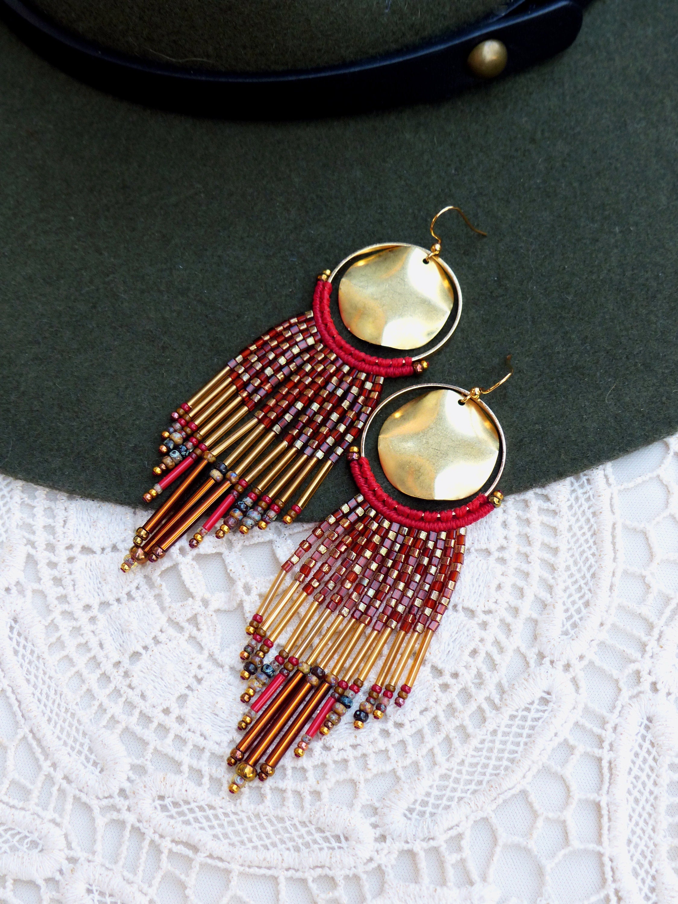 Peut inclure: Une paire de longues boucles d'oreilles en perles avec des accents dorés et rouges. Les boucles d'oreilles présentent un grand disque rond en or au sommet et pendent avec une cascade de perles.