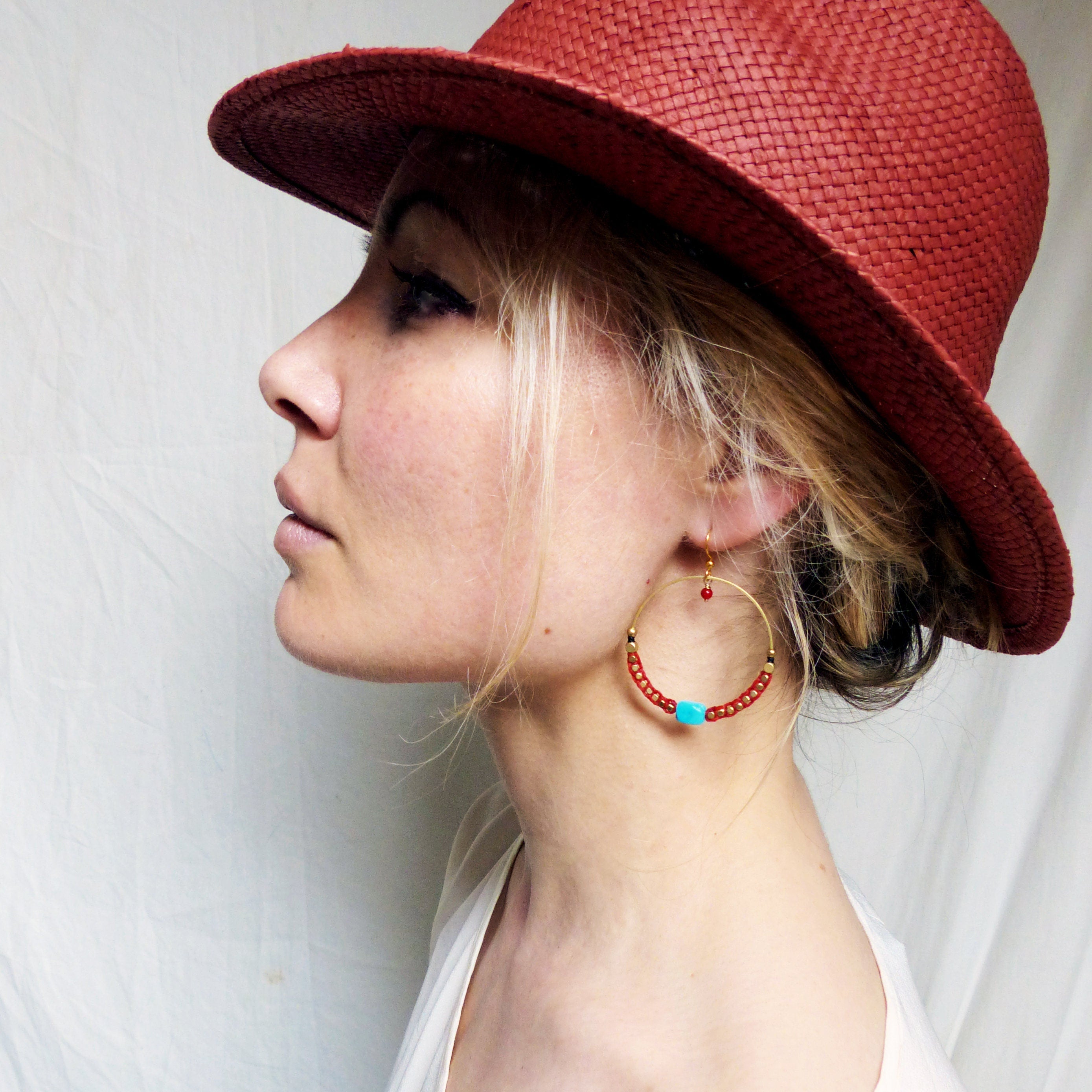 Peut inclure: Une femme portant un chapeau rouge à larges bords avec une boucle d'oreille en or avec des perles rouges et turquoise.