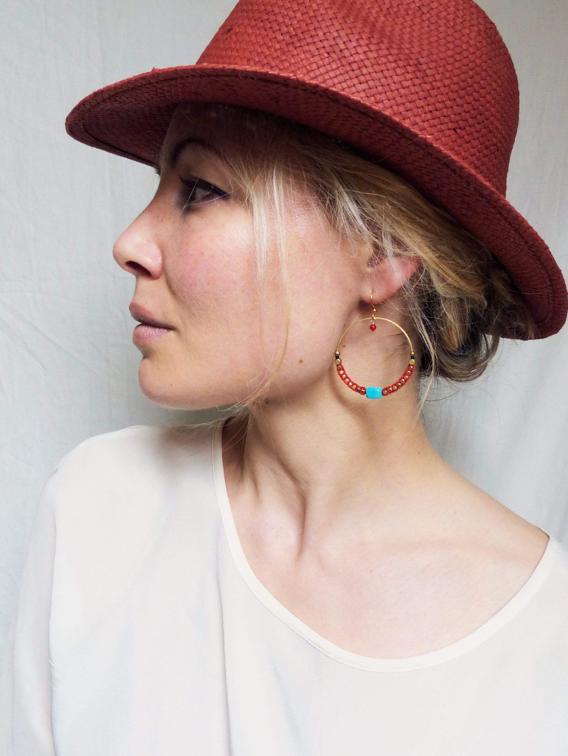 Peut inclure: Une femme portant un chapeau de paille rouge et une chemise blanche avec une paire de créoles dorées avec des perles turquoise et rouges.