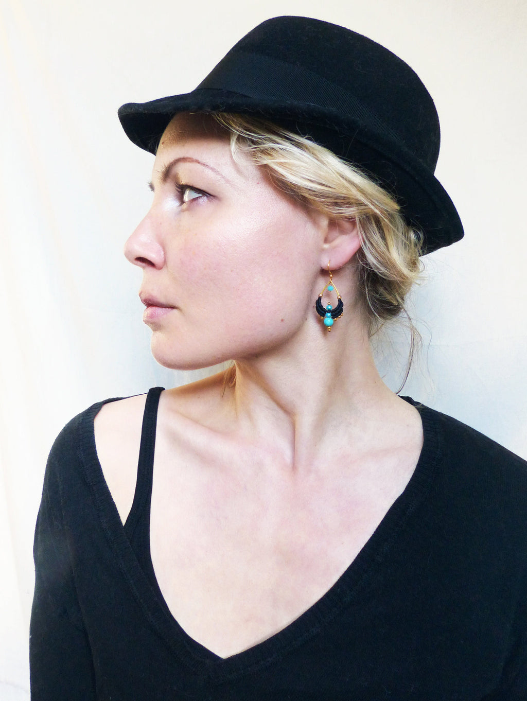 Peut inclure: Une femme portant un fedora noir et un pull noir à col en V avec une boucle d'oreille pendante turquoise et or.