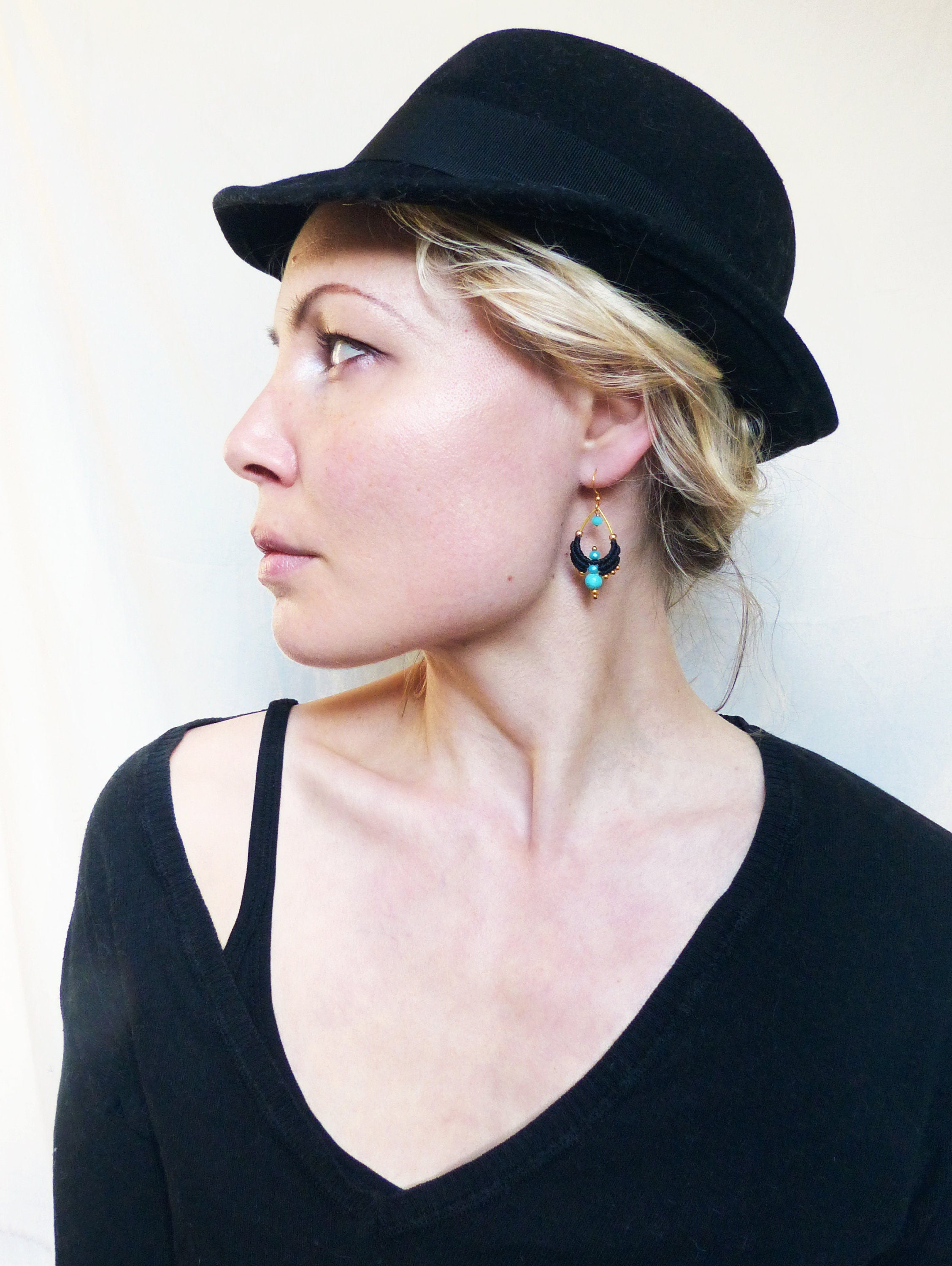 Peut inclure: Une femme portant un fedora noir et un pull noir à col en V avec une boucle d'oreille pendante turquoise et or.