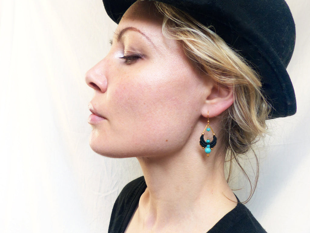 Peut inclure: Une femme portant un chapeau noir et un chemisier noir avec des boucles d'oreilles turquoise et dorées. Les boucles d'oreilles sont faites de fil noir et ont une forme de larme avec des perles turquoise.