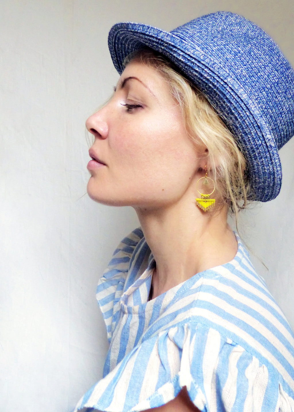 Peut inclure: Une femme portant une chemise rayée bleu et blanc avec un chapeau de paille bleu et des boucles d'oreilles en perles jaunes.