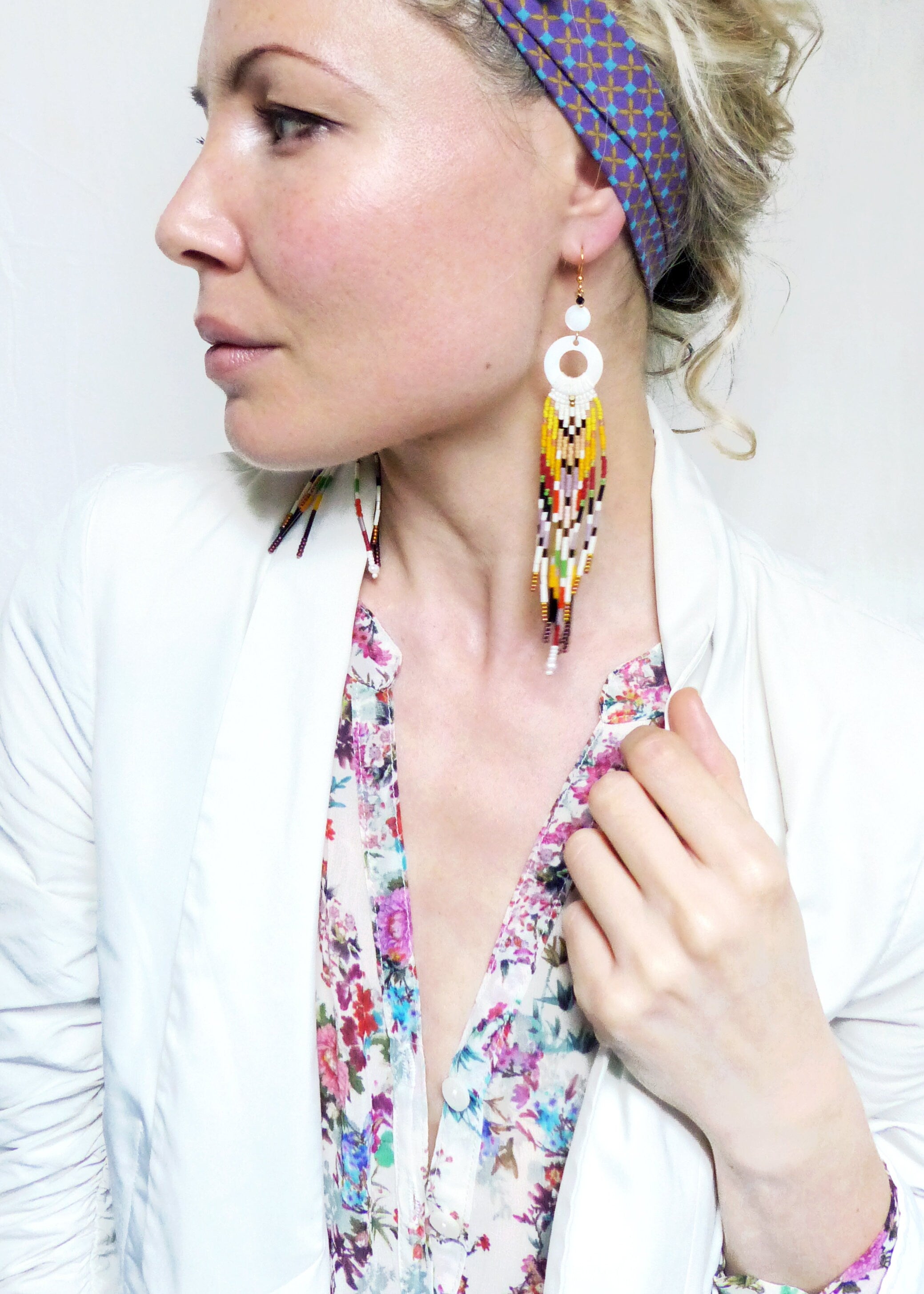 Peut inclure: Boucles d'oreilles en perles blanches avec un grand cercle blanc en haut et des perles colorées qui pendent. Les boucles d'oreilles sont portées par une personne avec un chemisier fleuri et un blazer blanc.
