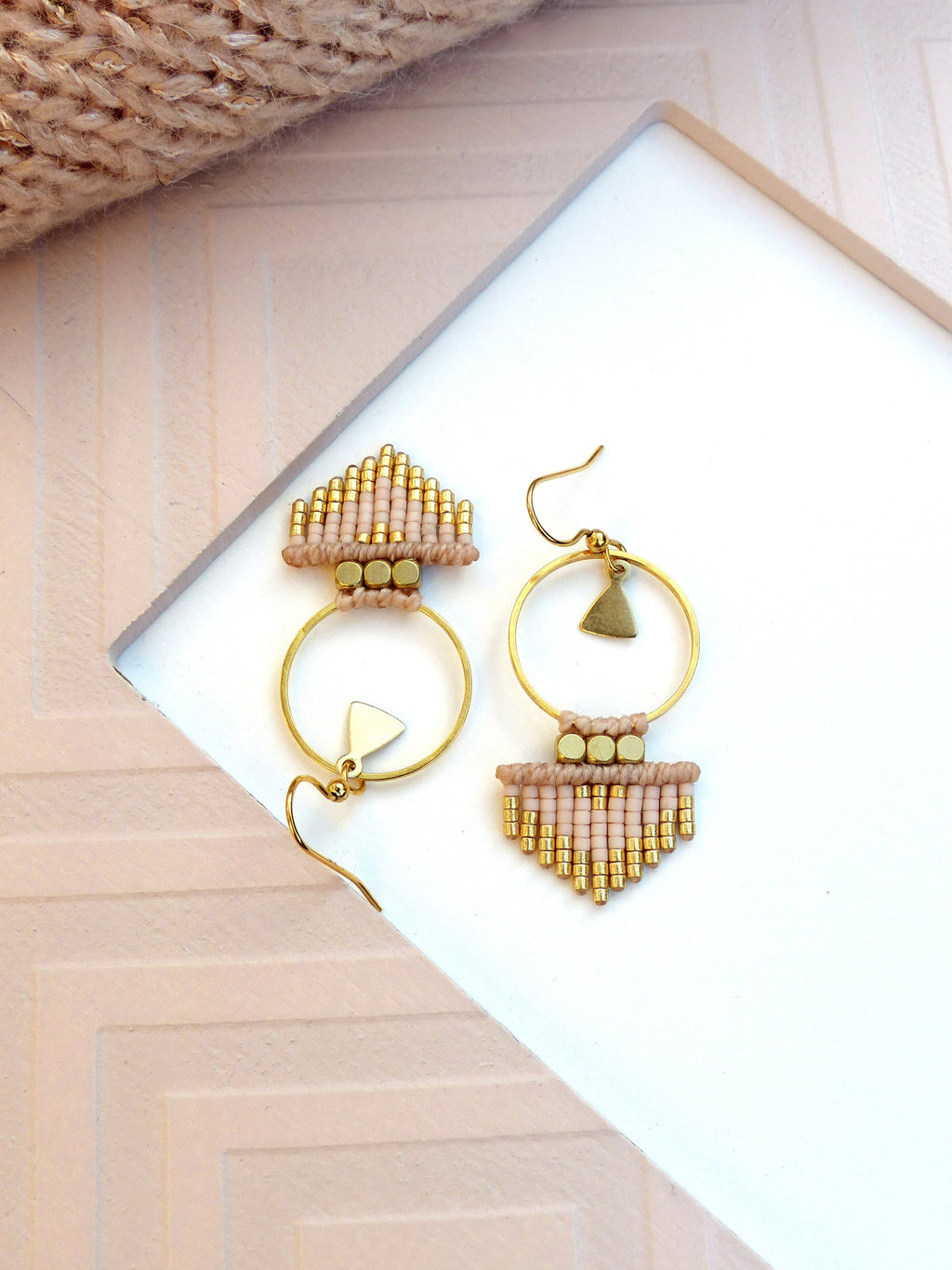 Peut inclure: Une paire de boucles d'oreilles créoles dorées avec une frange de perles roses et dorées et un petit charme triangulaire. 