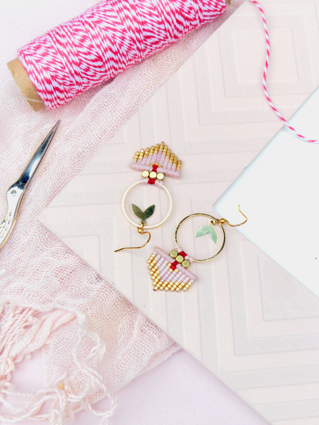 Peut inclure: Une paire de boucles d'oreilles créoles dorées avec des franges de perles roses et dorées. Les boucles d'oreilles ont un petit charme de feuille verte sur chaque créole.