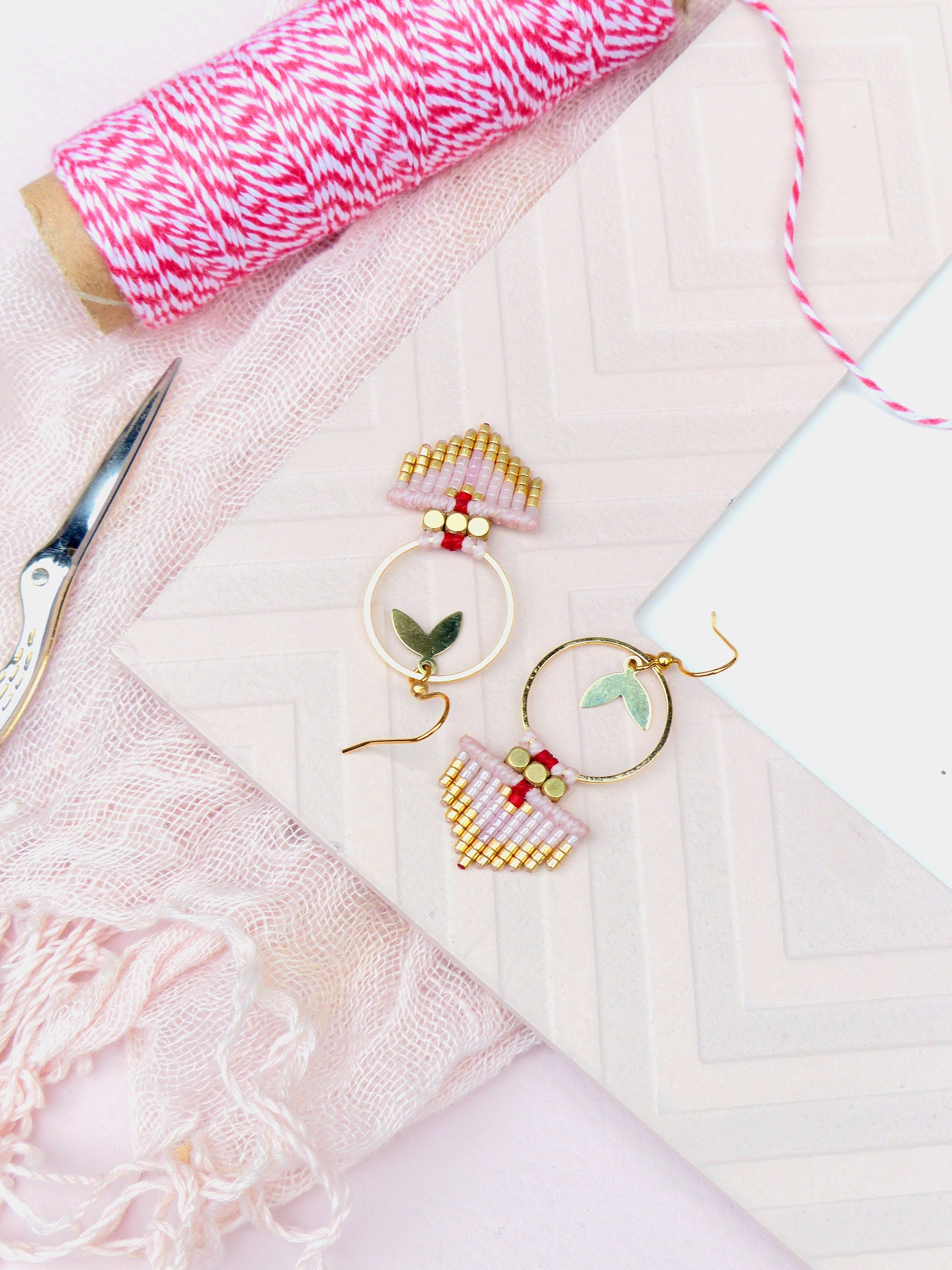 Peut inclure: Une paire de boucles d'oreilles créoles dorées avec des franges de perles roses et dorées. Les boucles d'oreilles ont un petit charme de feuille verte sur chaque créole.