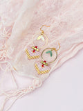 Peut inclure: Une paire de boucles d'oreilles en or avec des formes de goutte en perles roses et rouges et des cercles en or avec des accents de feuilles.