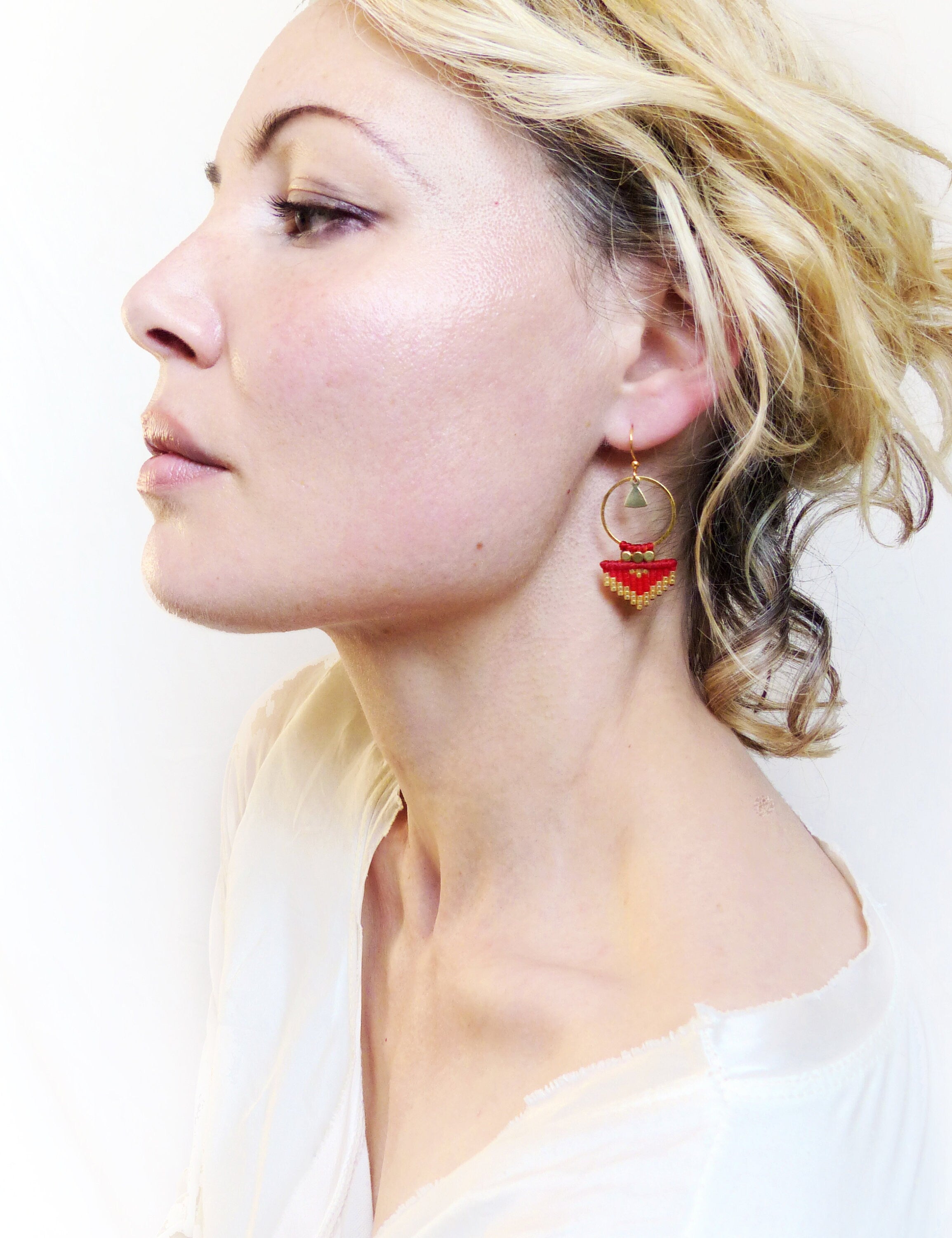 Peut inclure: Une paire de boucles d'oreilles créoles dorées avec un motif géométrique rouge et or. Les boucles d'oreilles pendent du lobe de l'oreille.