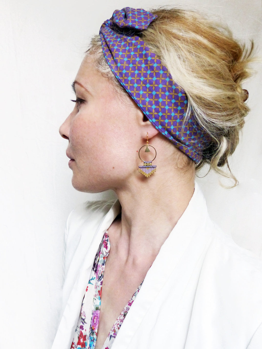 Peut inclure: Une femme portant un bandeau à motif violet et or avec une paire de boucles d'oreilles en perles violettes et dorées. Les boucles d'oreilles ont un design géométrique.