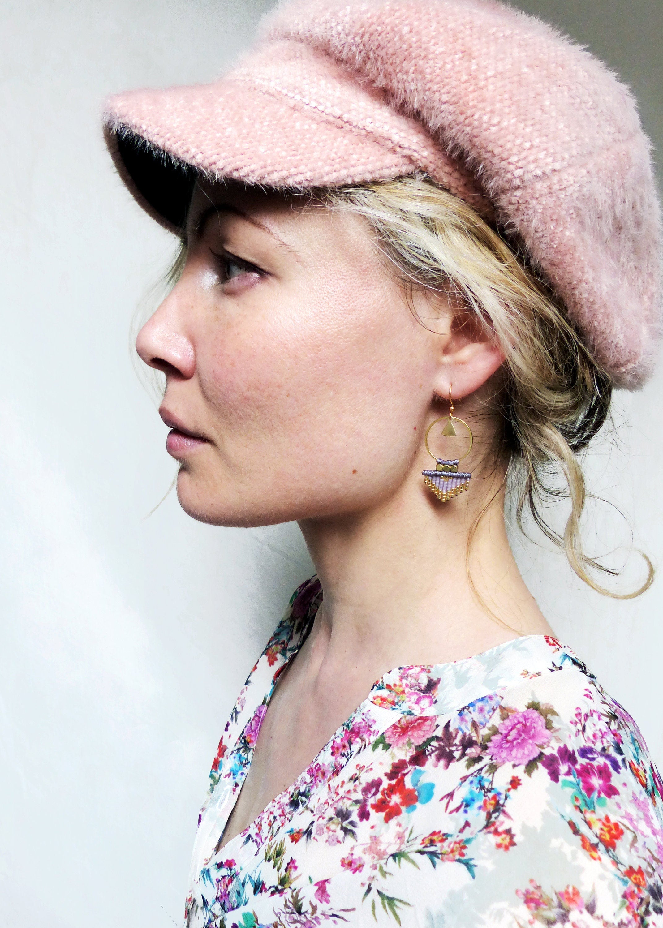 Peut inclure: Une femme portant une casquette de newsboy rose et une blouse à imprimé floral avec des boucles d'oreilles géométriques dorées et violettes.