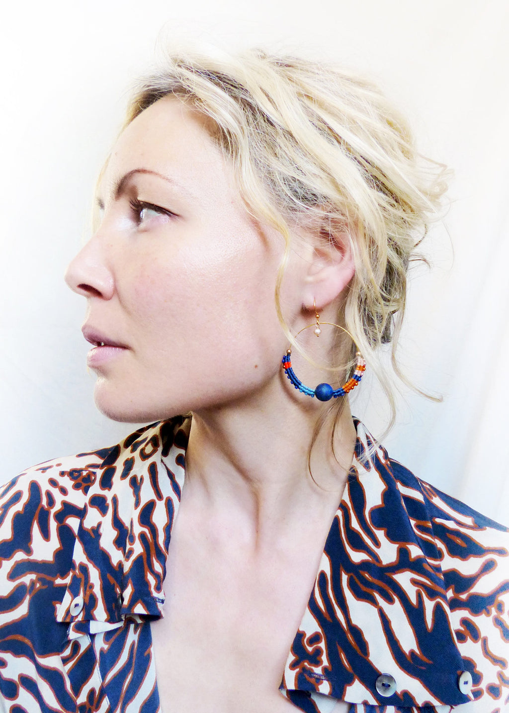 Peut inclure: Une femme portant une chemise à imprimé animal bleu et blanc avec de grandes boucles d'oreilles en forme de cerceau en perles bleues, orange et blanches.