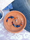 Peut inclure: Une paire de boucles d'oreilles créoles avec des détails en perles bleues, orange et roses. Chaque boucle d'oreille est ornée d'une grosse pierre bleu foncé.