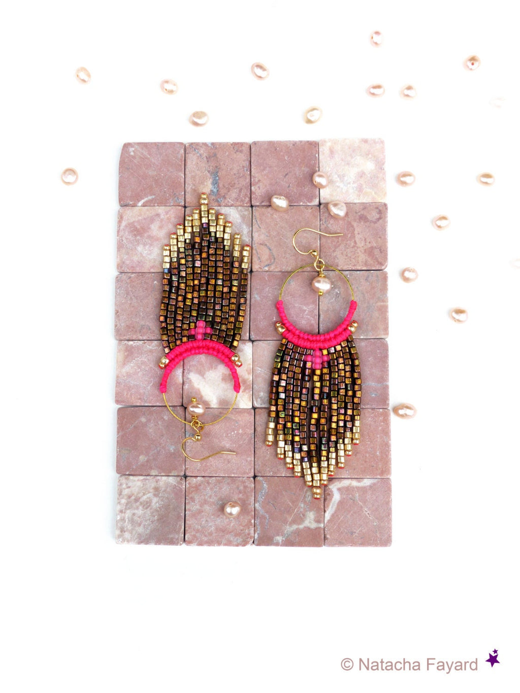 Peut inclure: Une paire de longues boucles d'oreilles en perles avec un pompon rose et des accents dorés. Les boucles d'oreilles sont suspendues à une surface carrelée.
